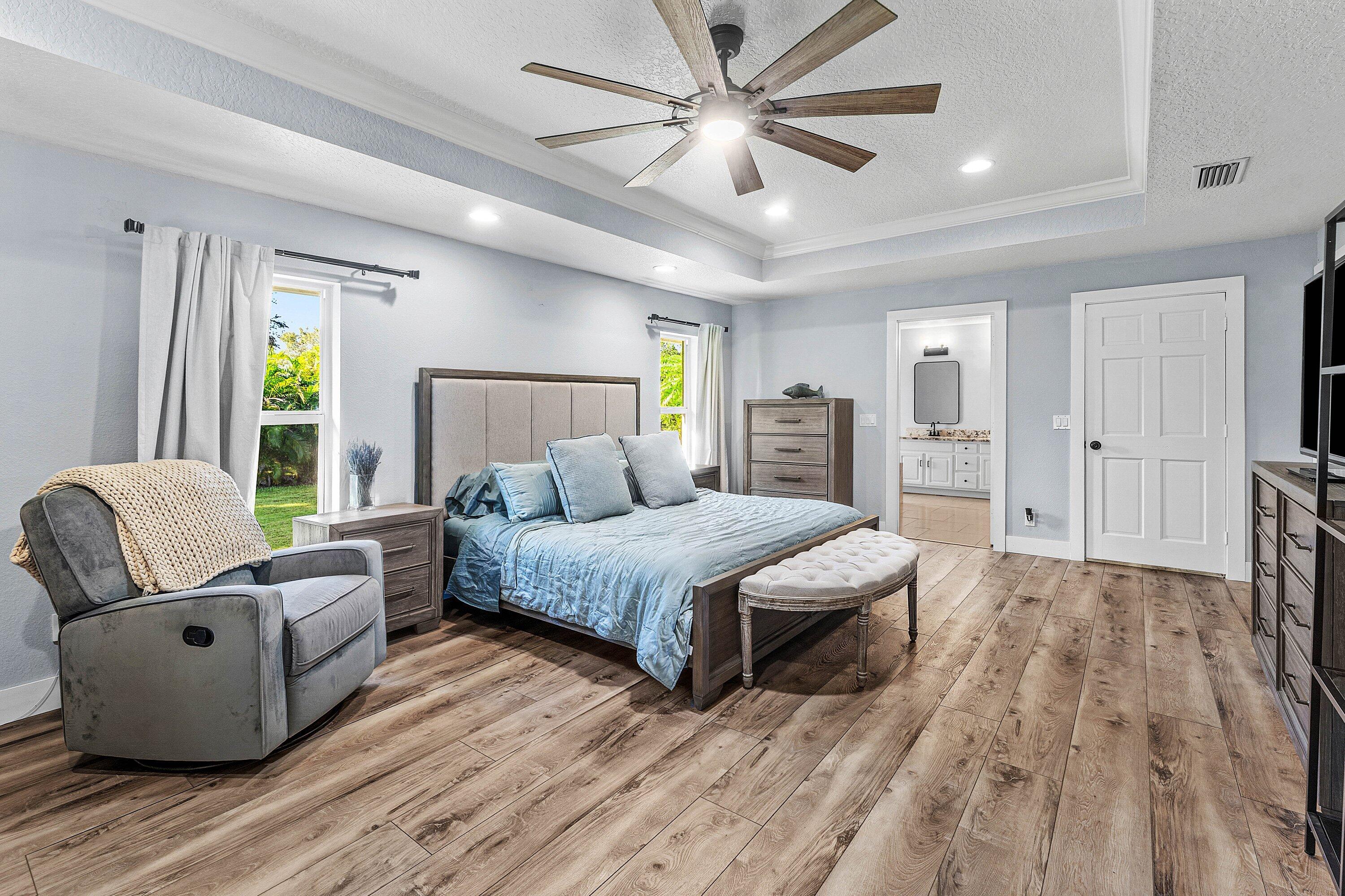 Tray ceiling with recessed lighting, multi-blade ceiling fan, and wood-finish flooring