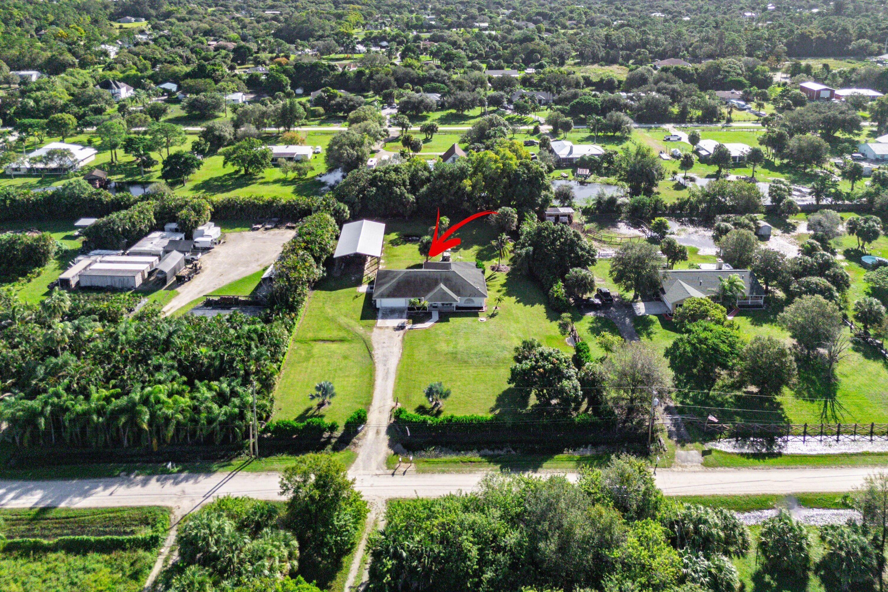Aerial perspective of a detached residence featuring a long private driveway, an expansive manicured lawn, and an auxiliary storage structure situated on a tree-lined lot