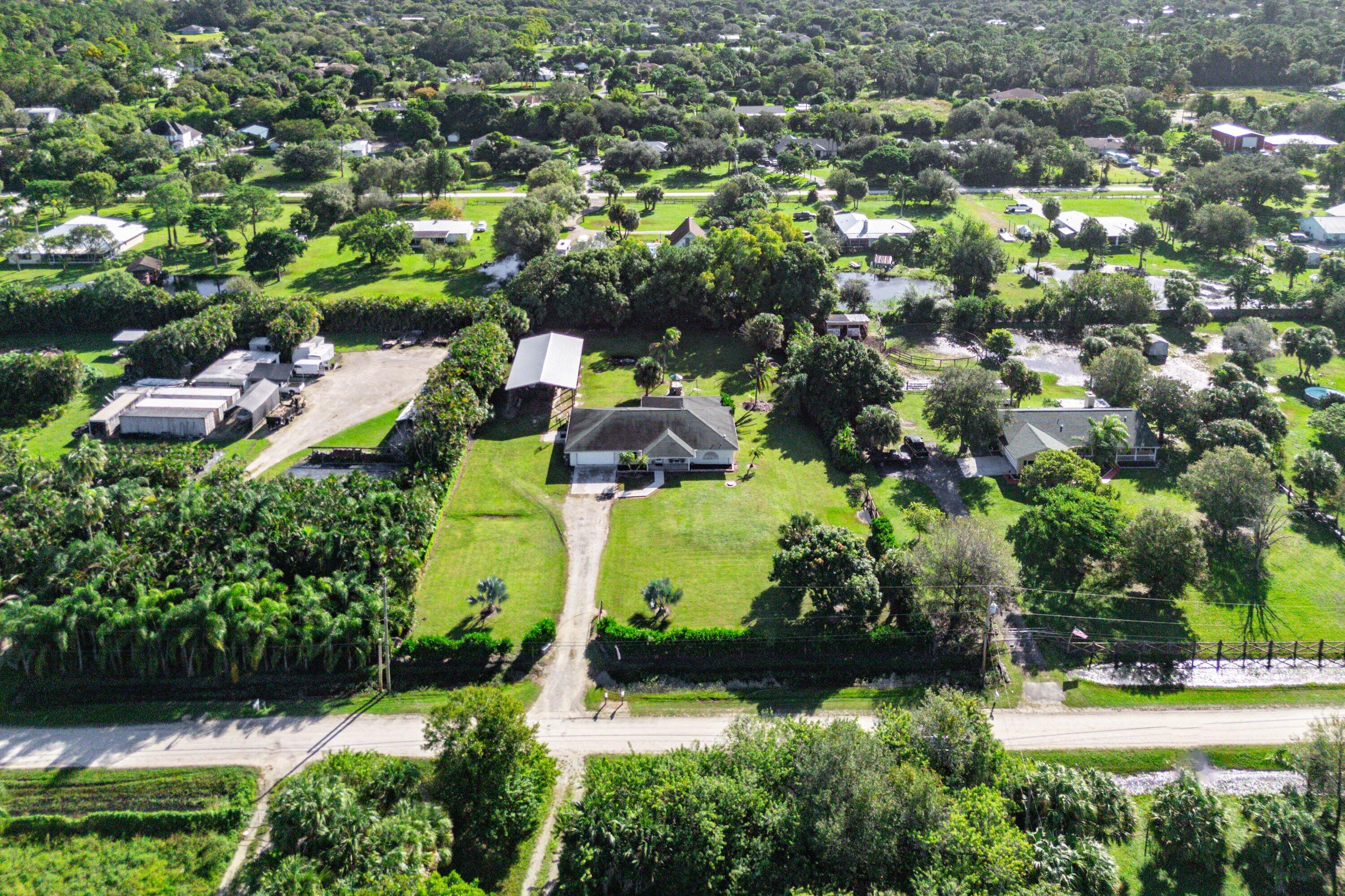 Aerial perspective of a sprawling property featuring a large residence, detached workshop, expansive open grounds, mature trees, and a long driveway