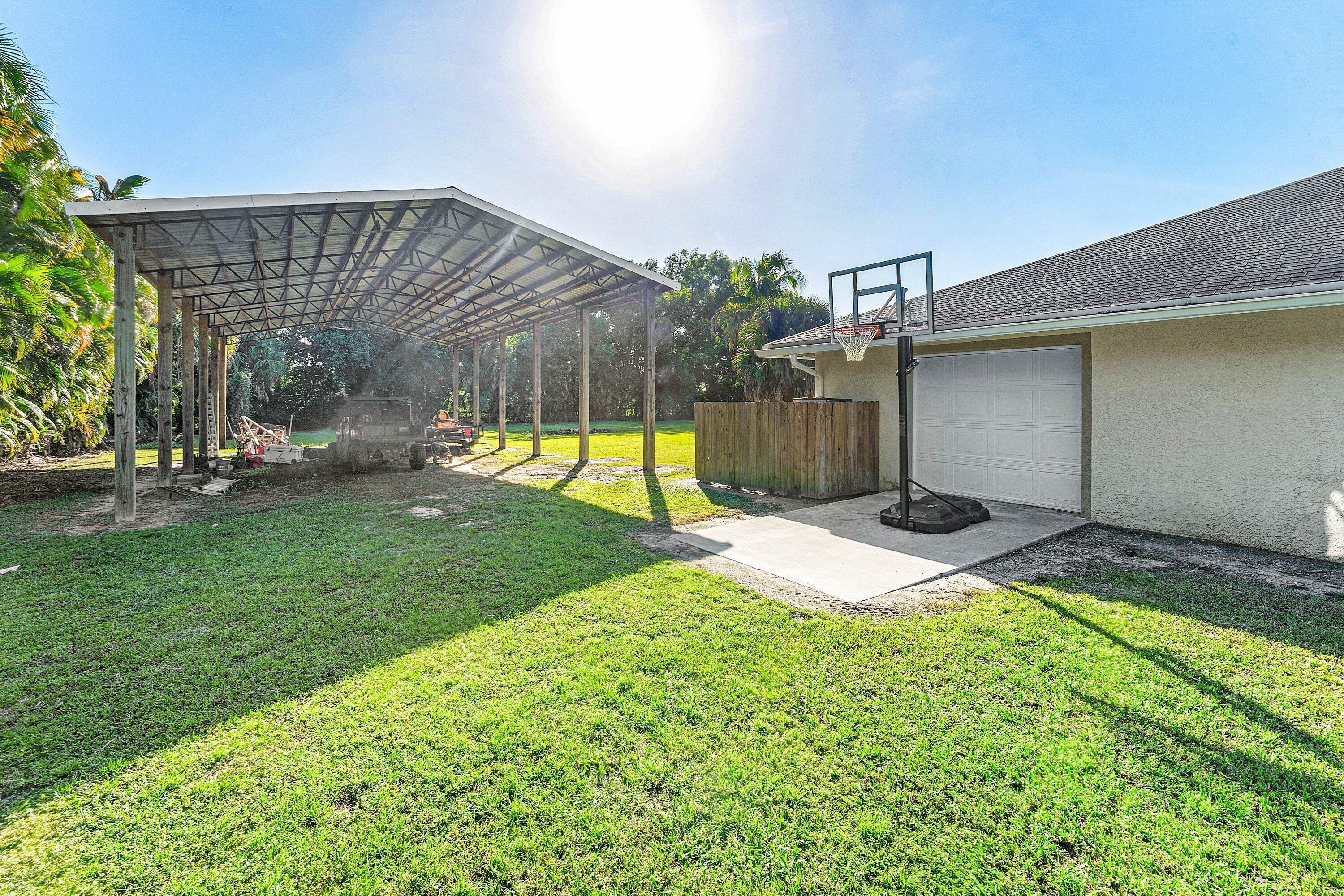 Exterior space featuring an expansive covered carport, a concrete pad, a garage, and a grass lawn