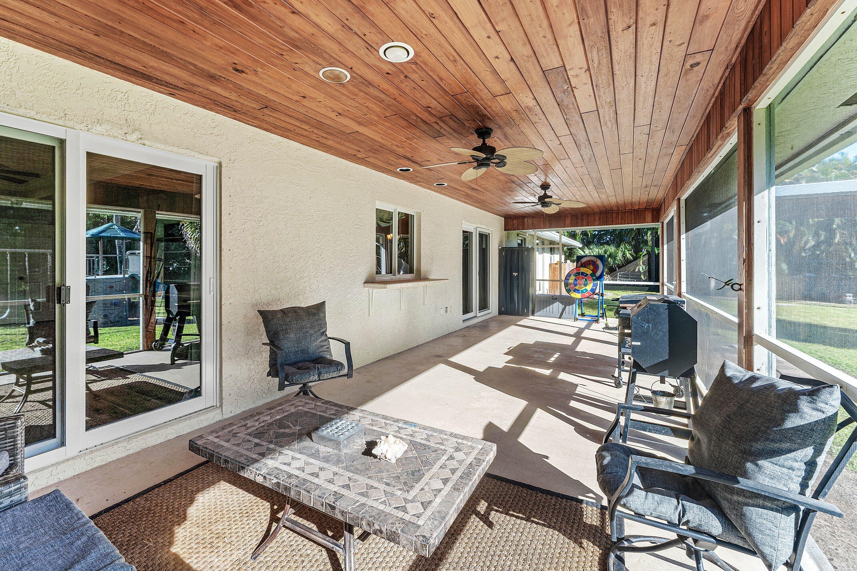 Screened patio featuring wood-paneled ceiling, dual ceiling fans, concrete flooring, and sliding glass door access