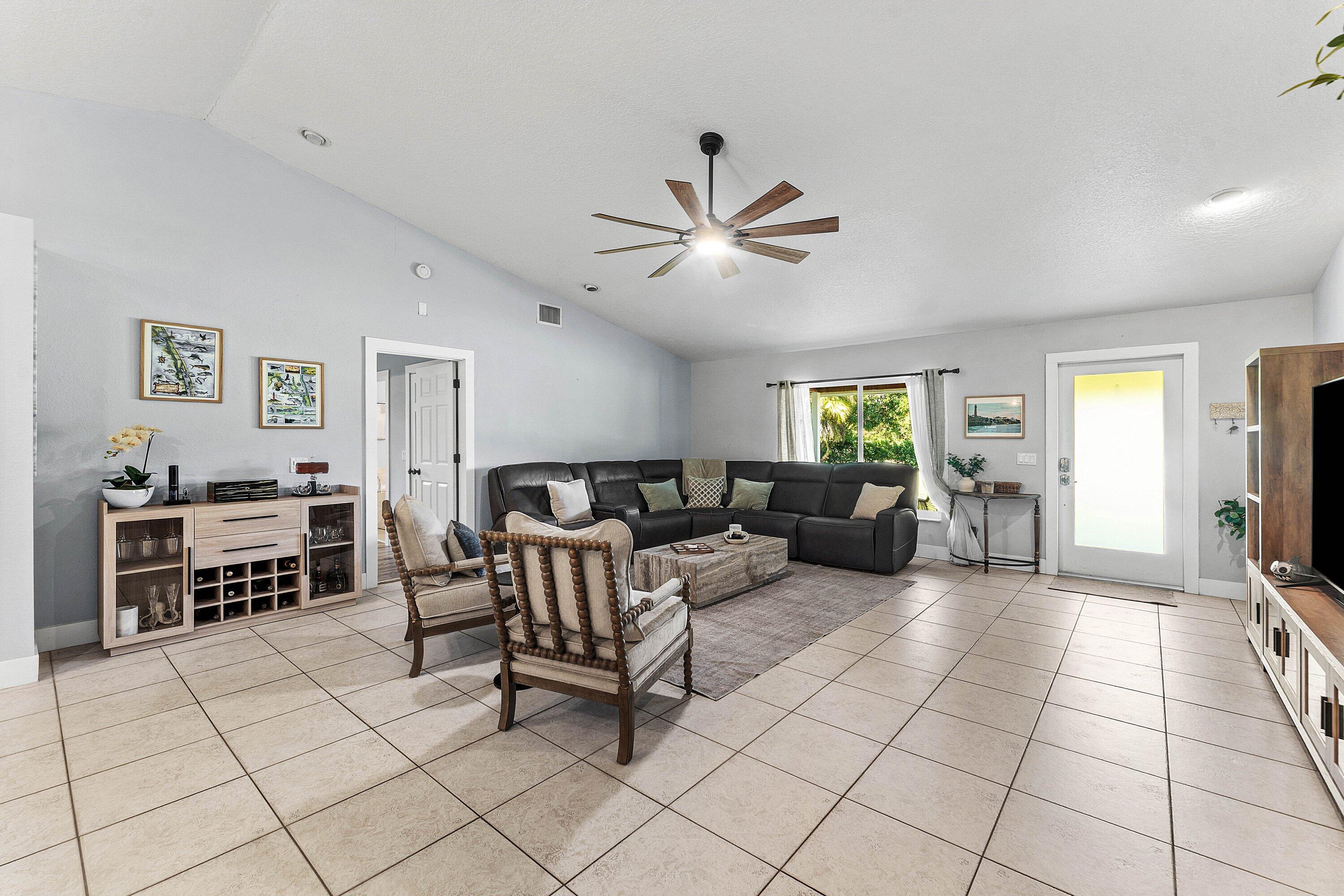 Living area featuring vaulted ceilings, large-format tile flooring, a multi-blade ceiling fan, and a glass-panel entry door