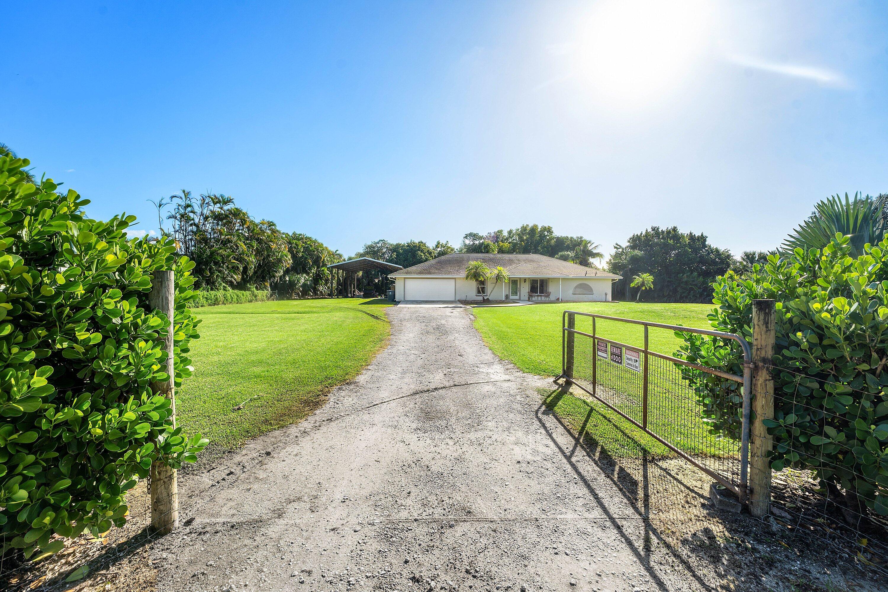 Single-story residence featuring a gated gravel entrance, expansive manicured lawn, and detached carport