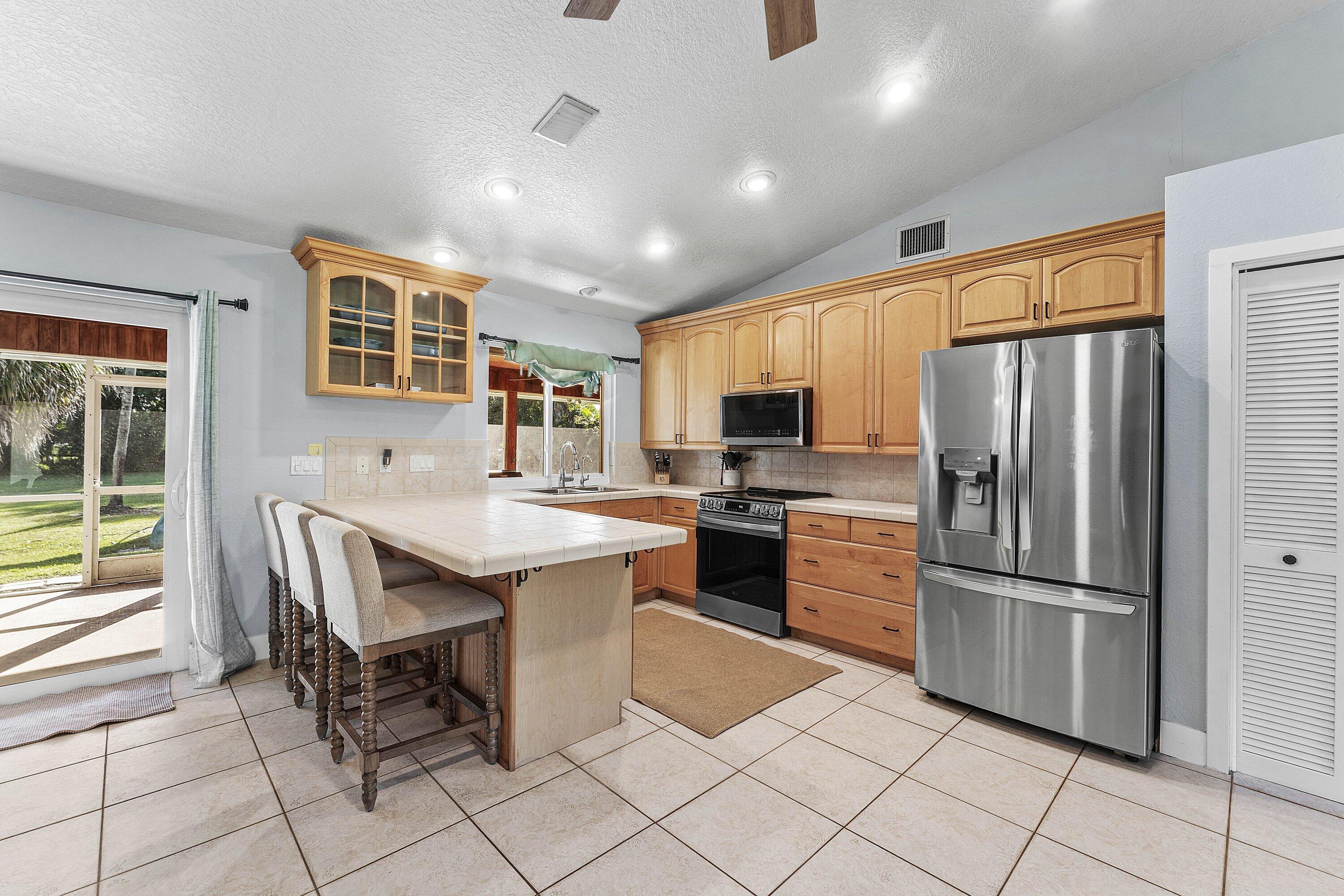 Kitchen featuring wooden cabinetry, tiled countertops, stainless steel appliances, recessed lighting, and tile flooring