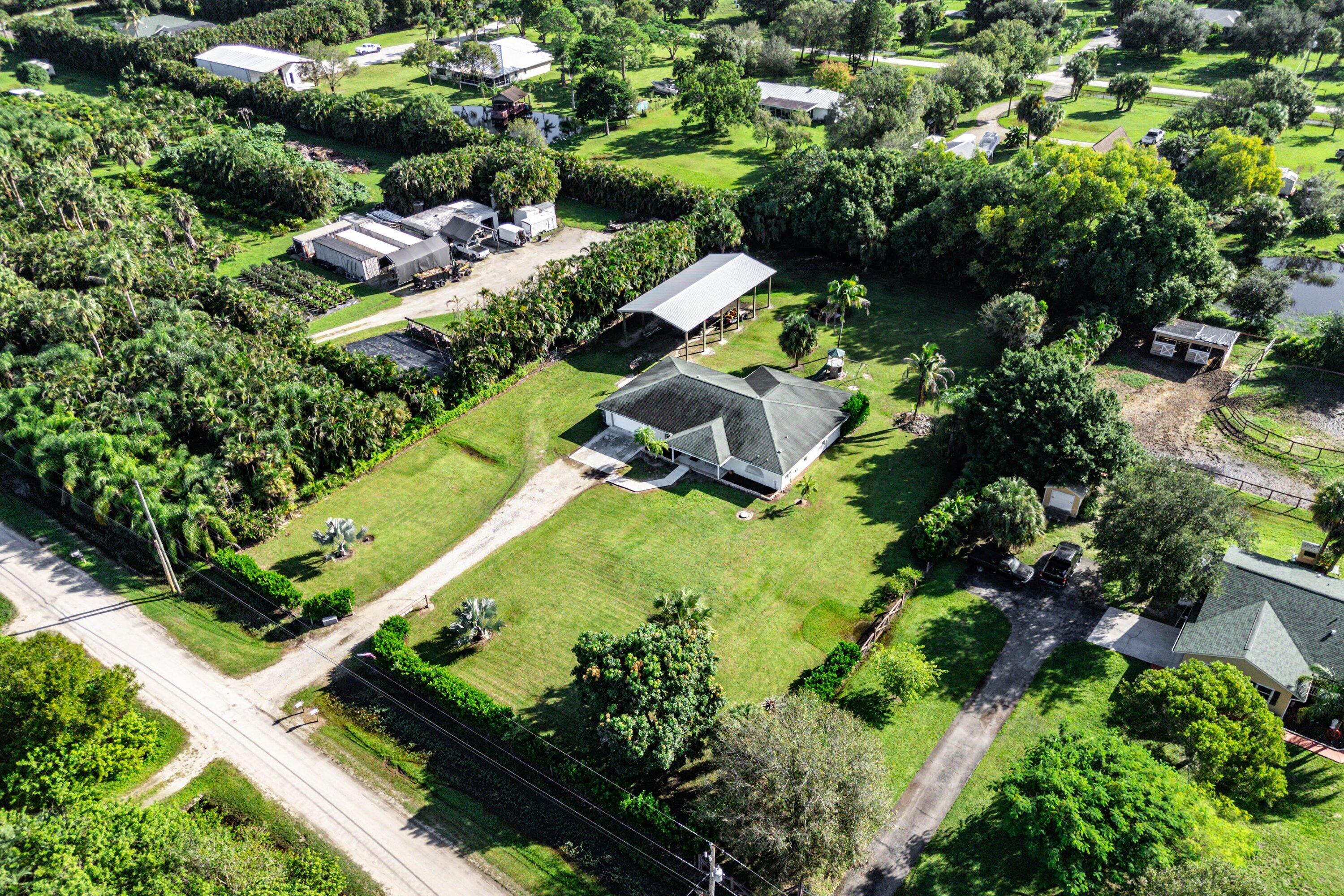 Aerial perspective featuring a multi-gabled roofline, expansive grass acreage, a detached metal-frame carport, and mature perimeter landscaping