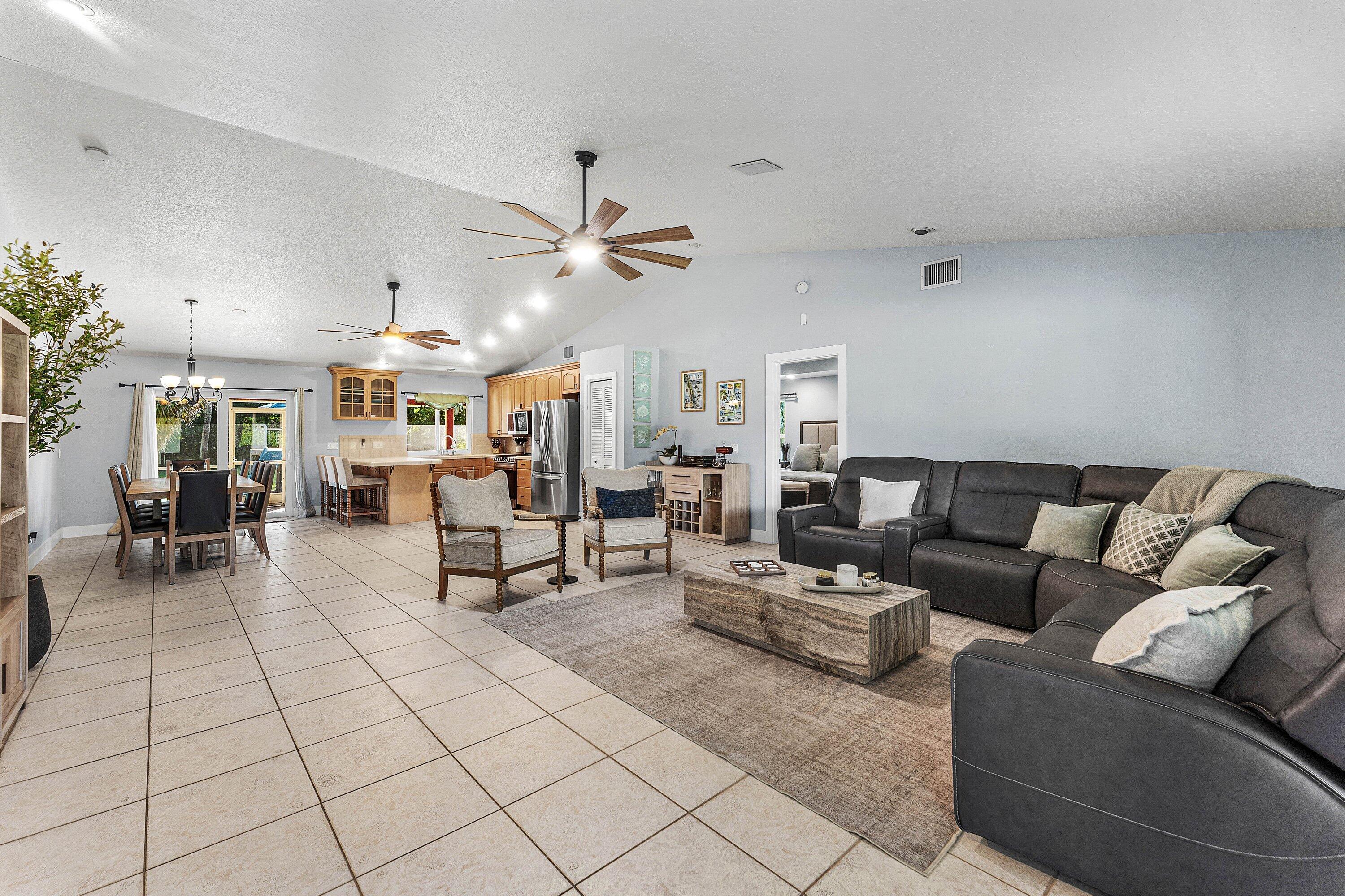 Open-concept interior featuring vaulted ceilings, light-toned ceramic tile flooring, dual ceiling fans, and recessed lighting