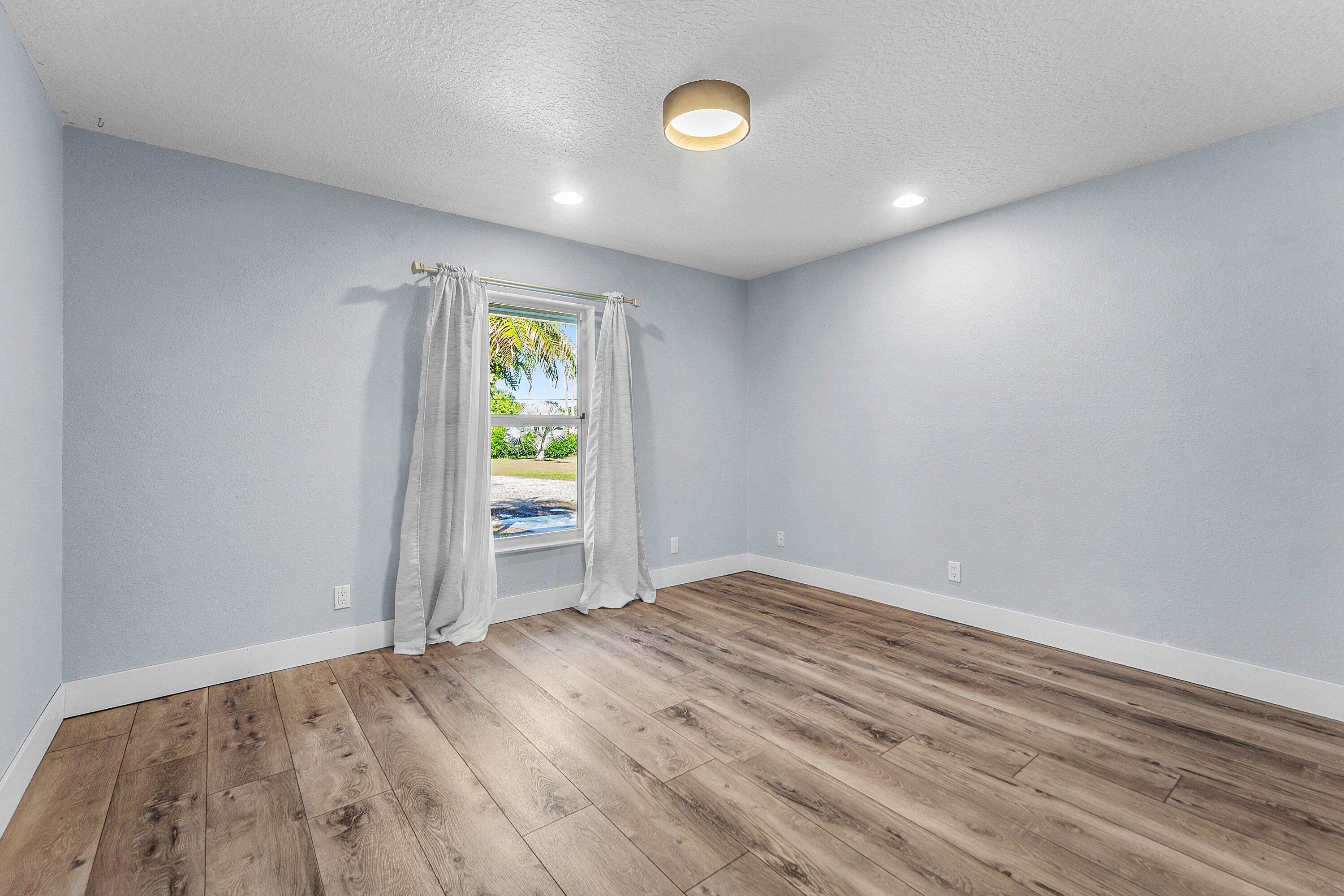 Interior room featuring wood-finish flooring, neutral wall tones, a single window, and a drum-style ceiling light fixture
