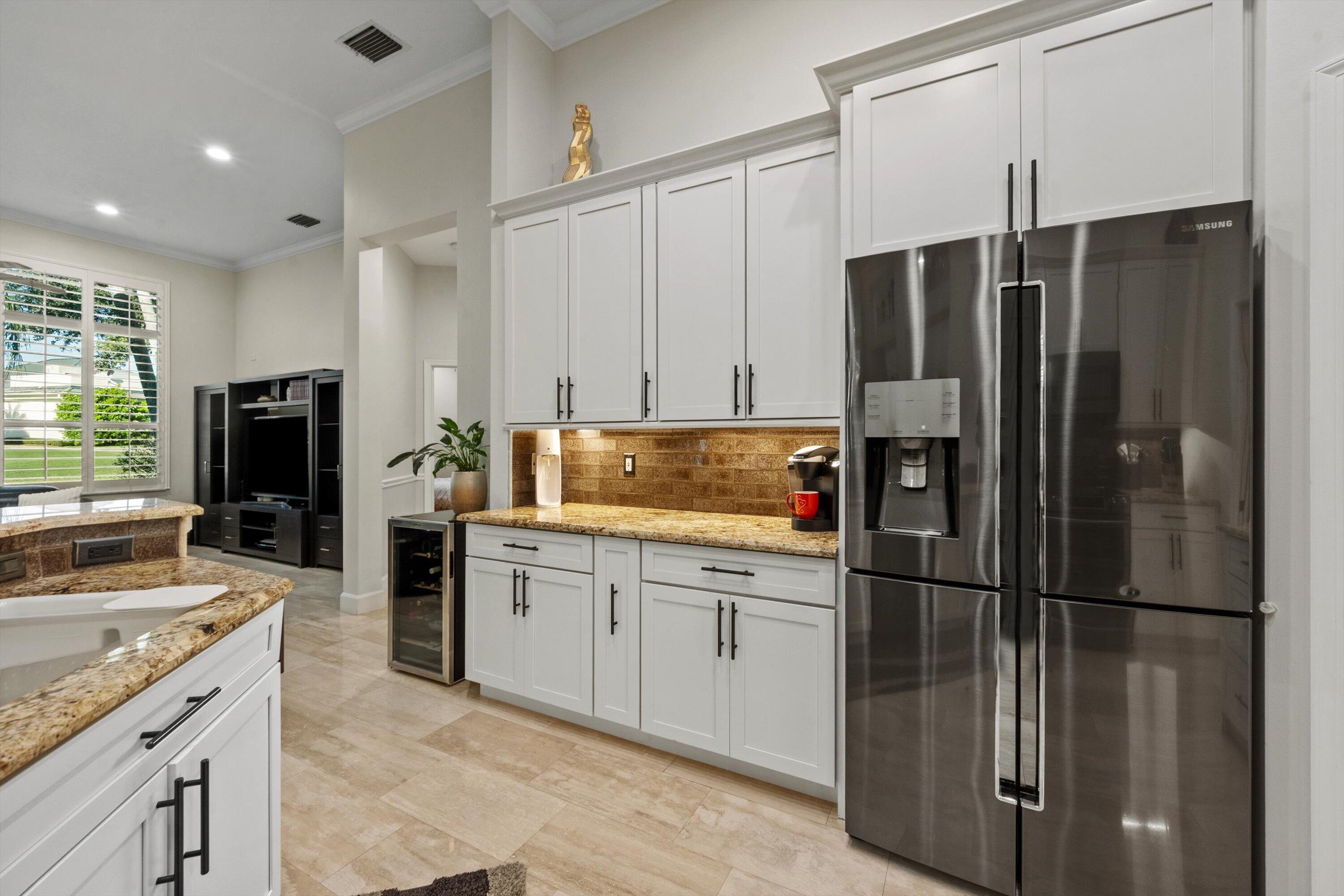 Kitchen featuring white cabinetry with matte black hardware, stone-finish countertops, tiled backsplash, stainless steel refrigerator, and stone-finish flooring