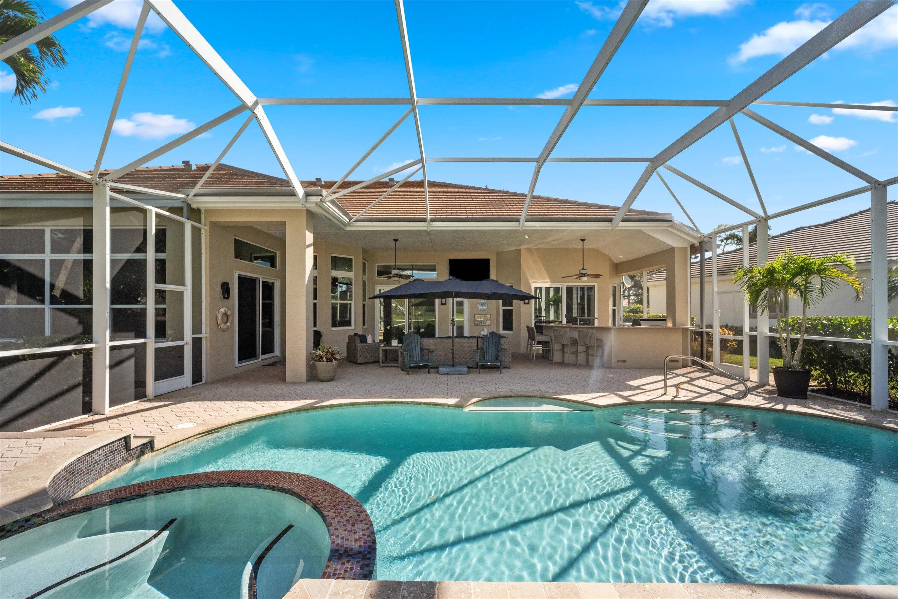 Screen-enclosed patio featuring a paver deck, built-in outdoor bar, in-ground pool, and integrated spa