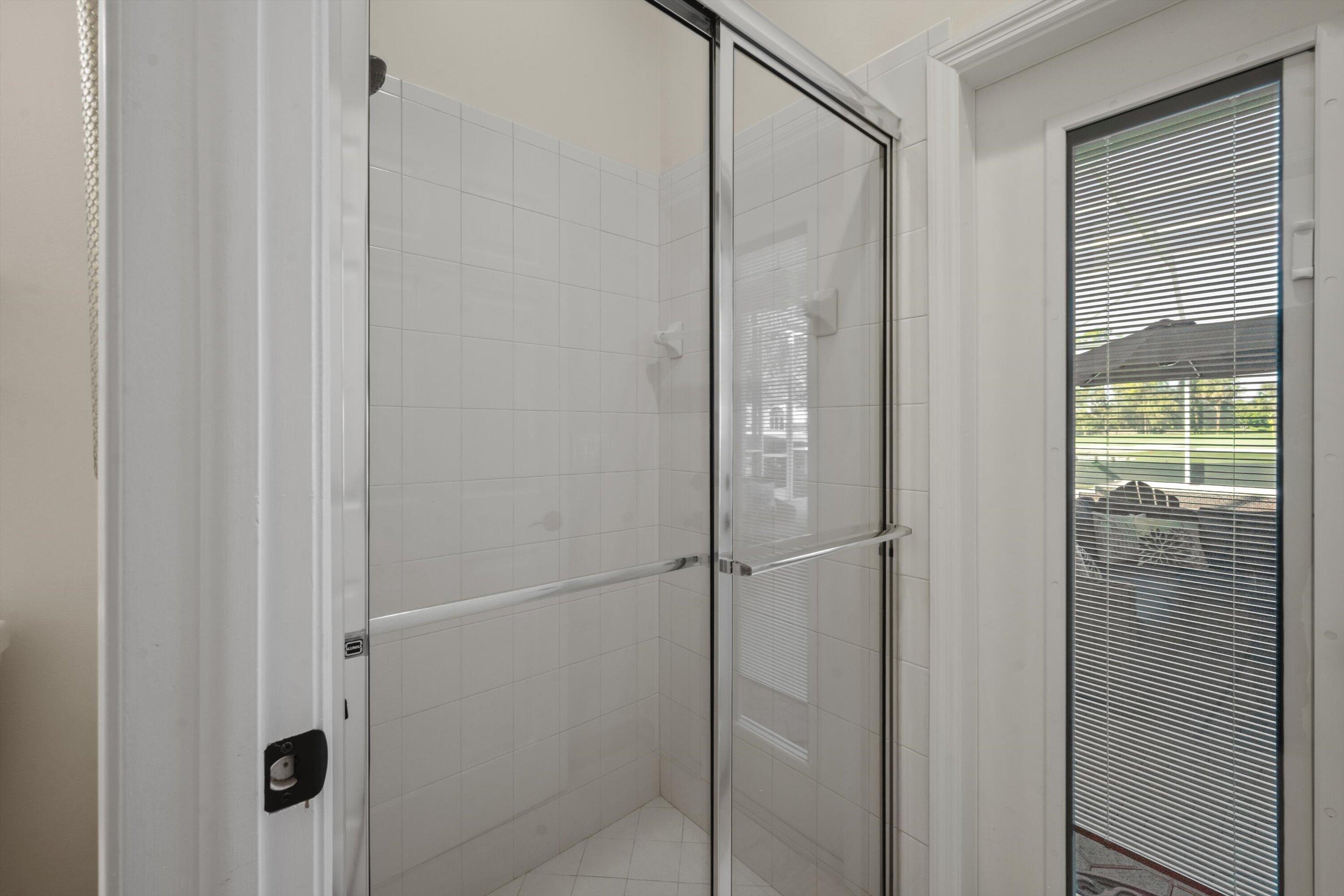 Shower enclosure featuring a chrome-framed sliding glass door, white tiled walls, and an exterior door with integrated blinds