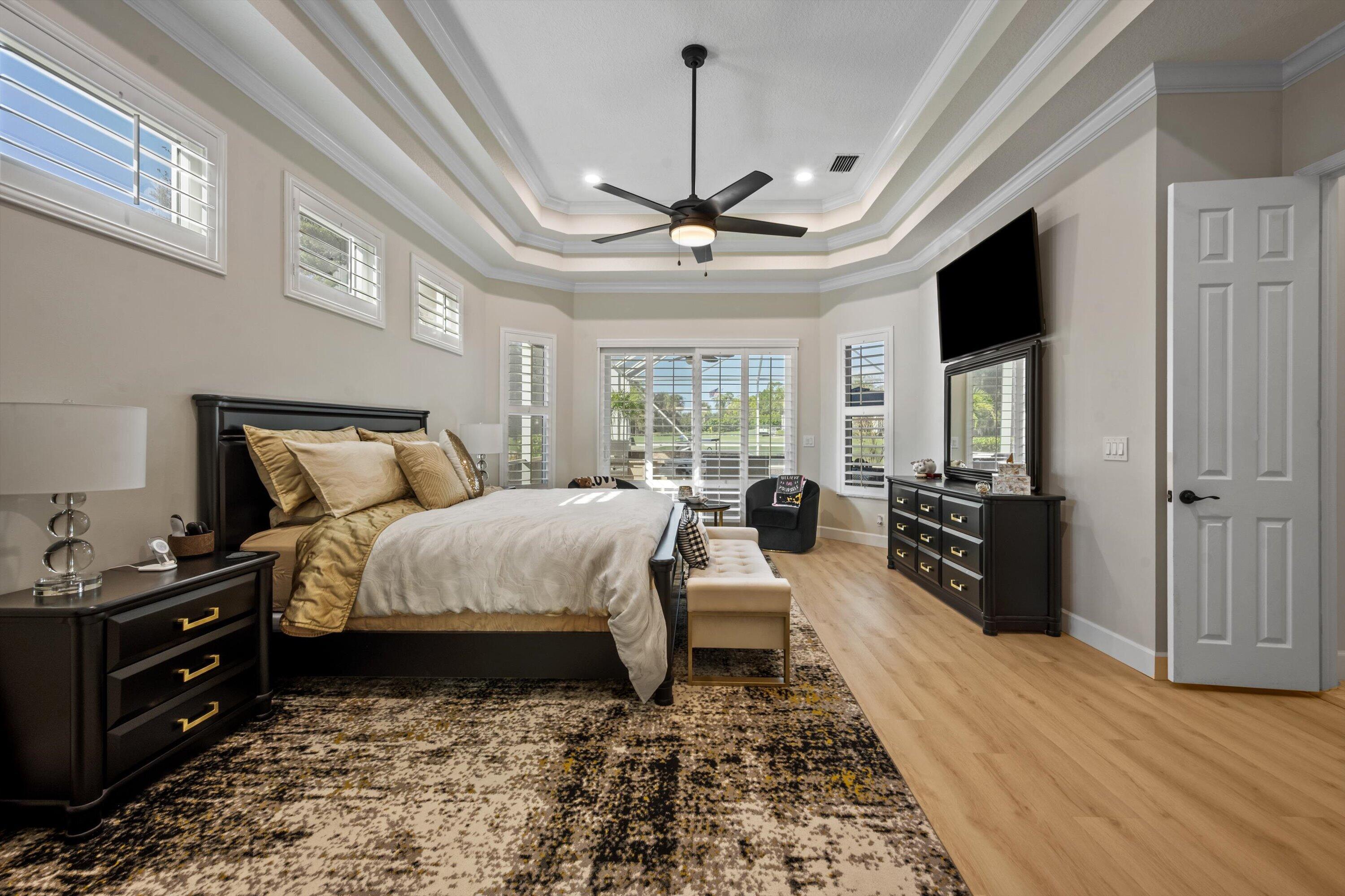 Tray ceiling with crown molding, wood-finish flooring, central ceiling fan, and multiple plantation-style shutters