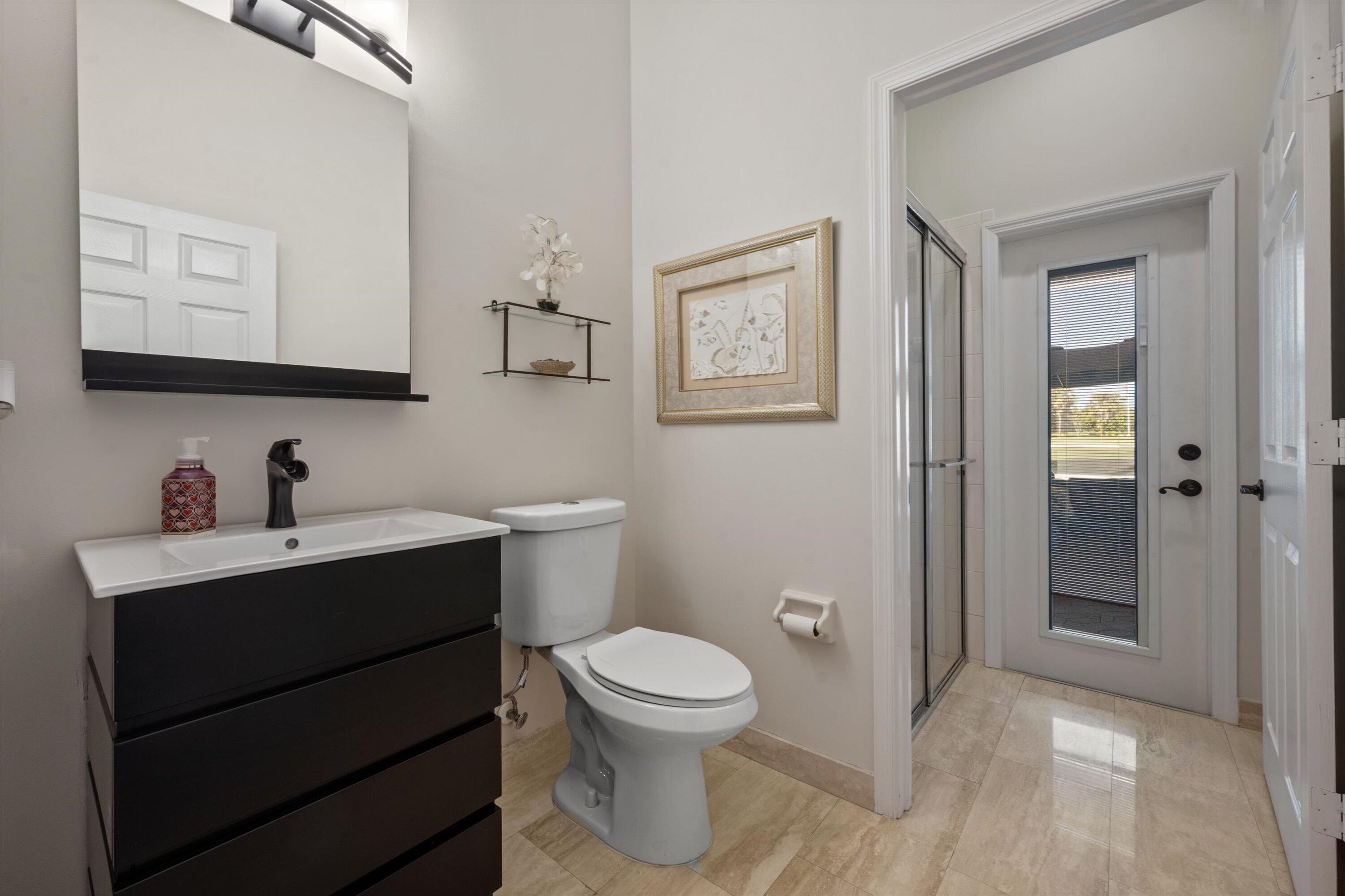 Bathroom featuring a vanity with dark-finish cabinetry, a rectangular vessel sink, and a matte black faucet, complemented by polished stone-finish flooring and a glass-enclosed shower