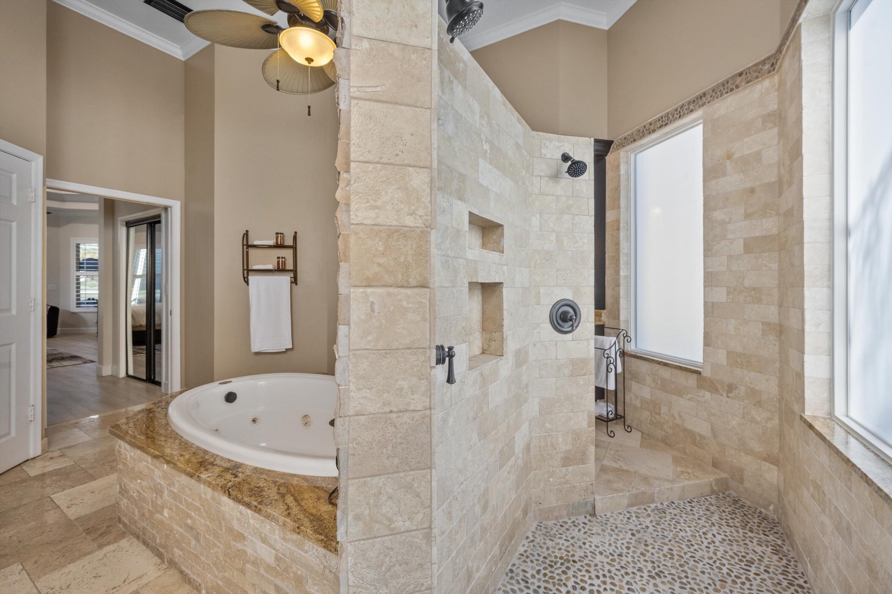 Bathroom featuring a jetted soaking tub with a stone-finished deck, walk-in shower with natural stone tile walls, pebble floor inlay, and recessed wall niches
