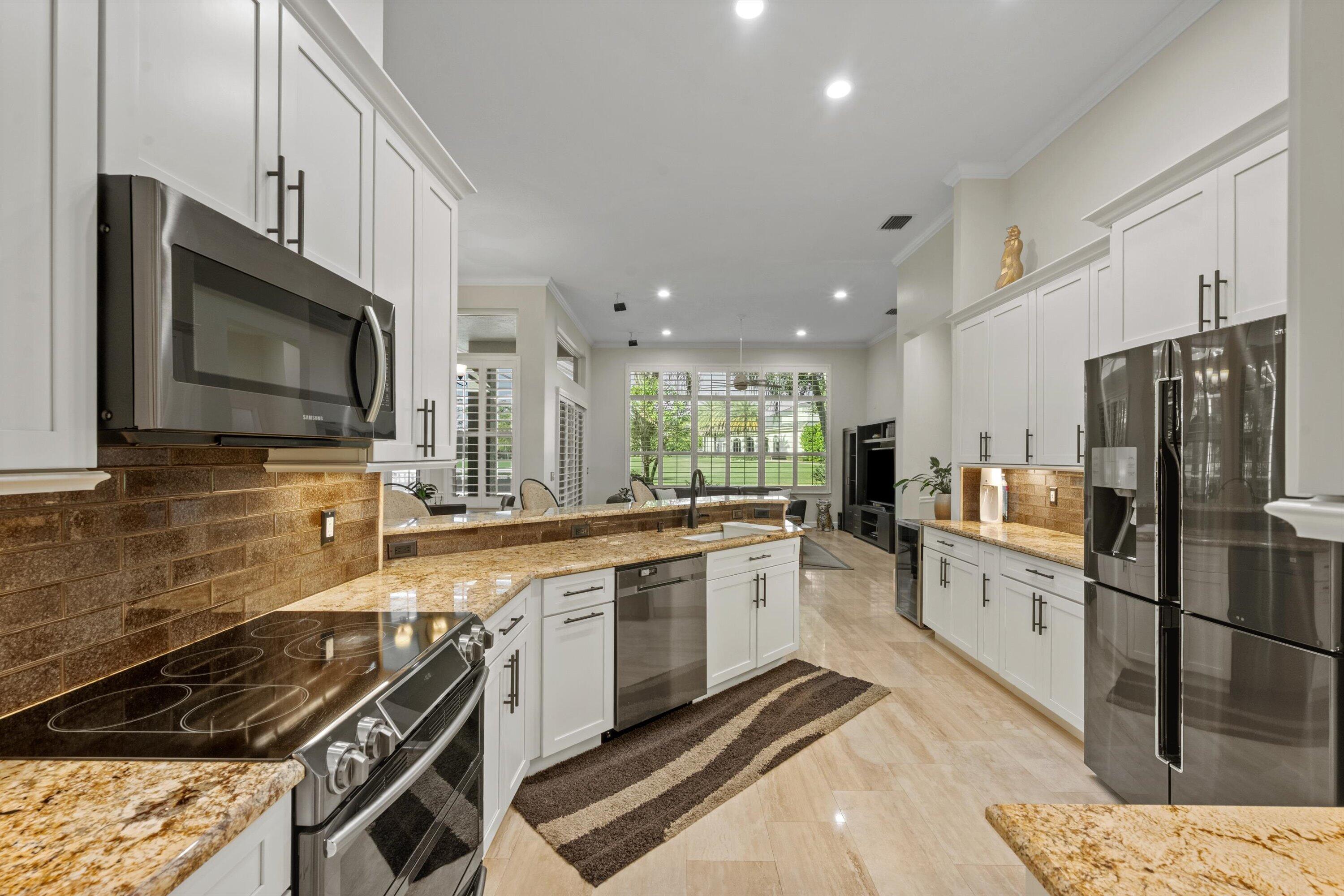 Kitchen featuring white cabinetry with dark hardware, stone-finish countertops, brick-style tile backsplash, stainless steel appliances, and tile flooring