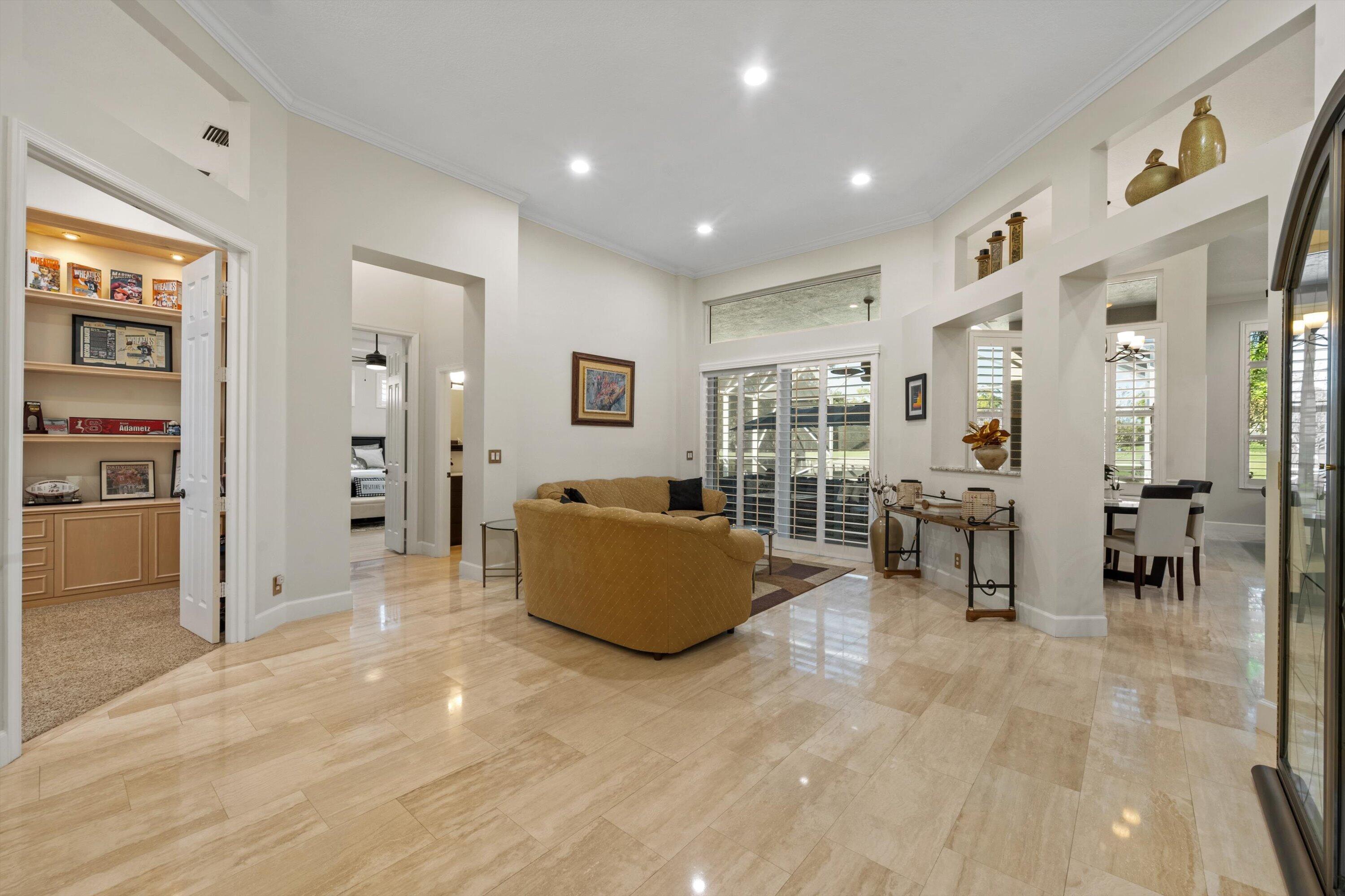 High-ceiling living area featuring large-format tile flooring, built-in recessed wall shelving, a transom window, and sliding glass doors