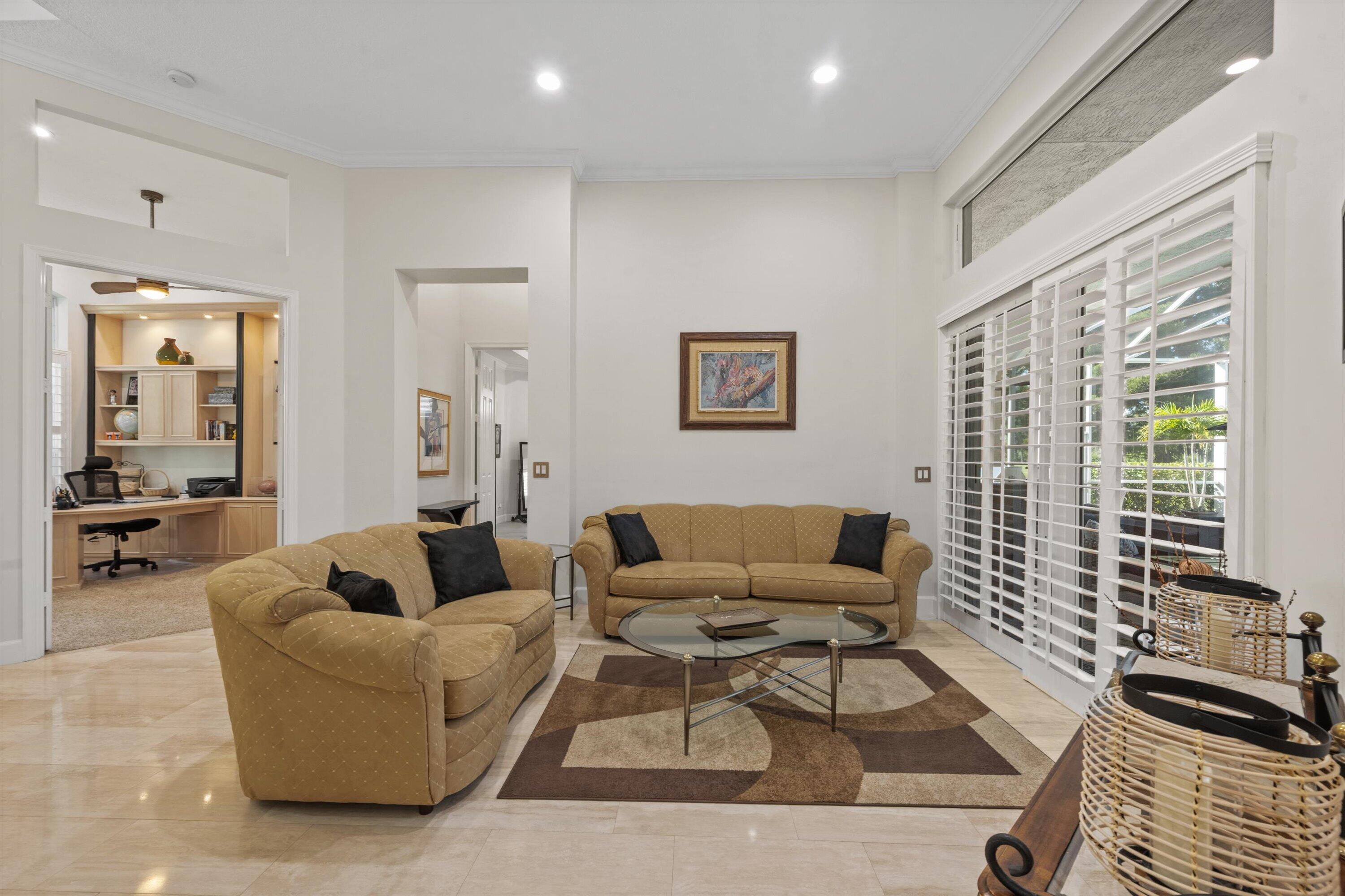 High-ceiling living area featuring neutral tile flooring, recessed lighting, and expansive sliding glass doors with plantation shutters