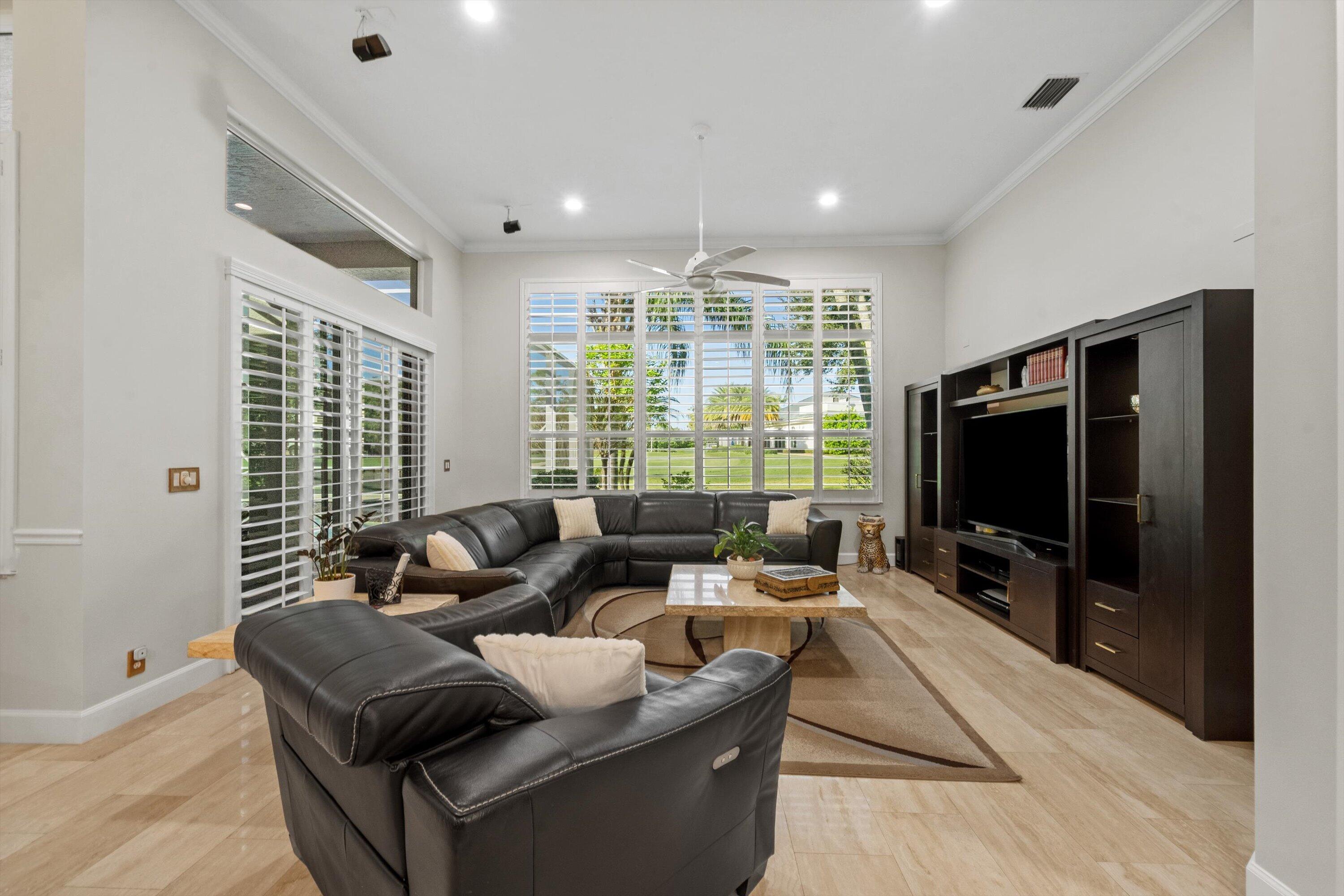 High ceilings with recessed lighting, oversized windows with plantation shutters, light-toned flooring, and built-in cabinetry