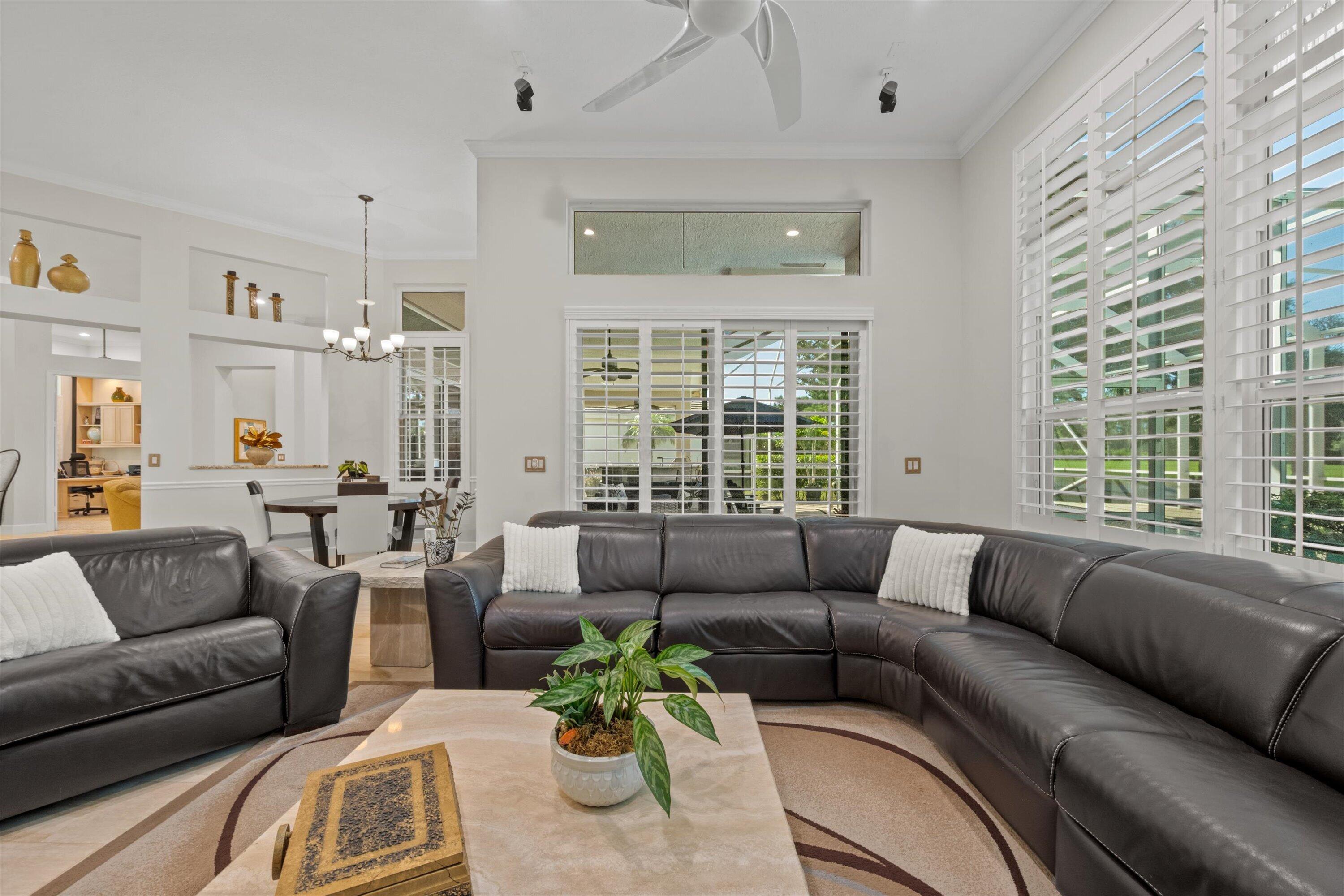 High ceilings featuring a multi-blade ceiling fan, expansive transom windows, built-in wall niches, custom plantation shutters, and sliding glass doors