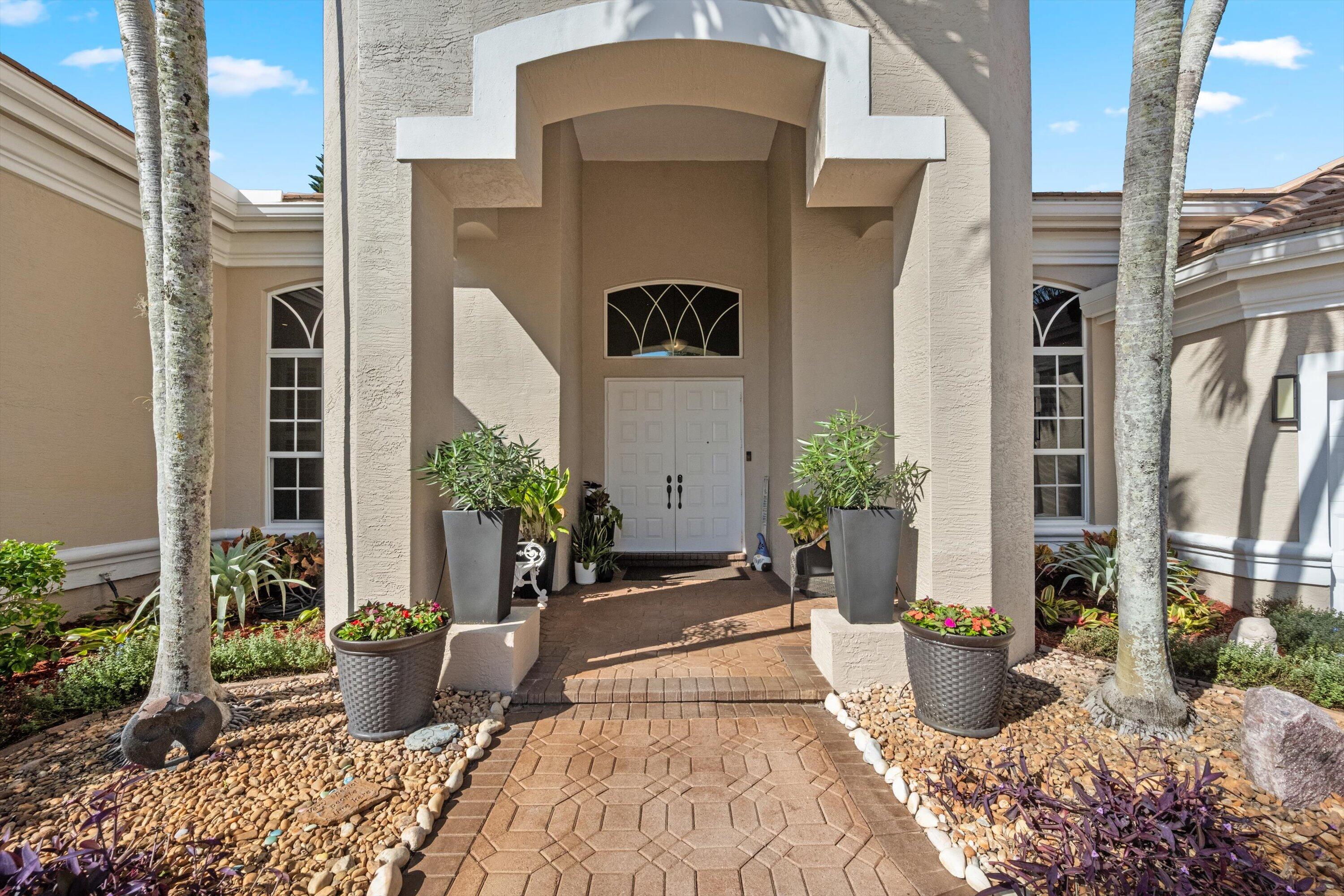 Stucco exterior featuring a covered entryway with arched transom window, dual-paneled entry doors, and patterned paver walkway