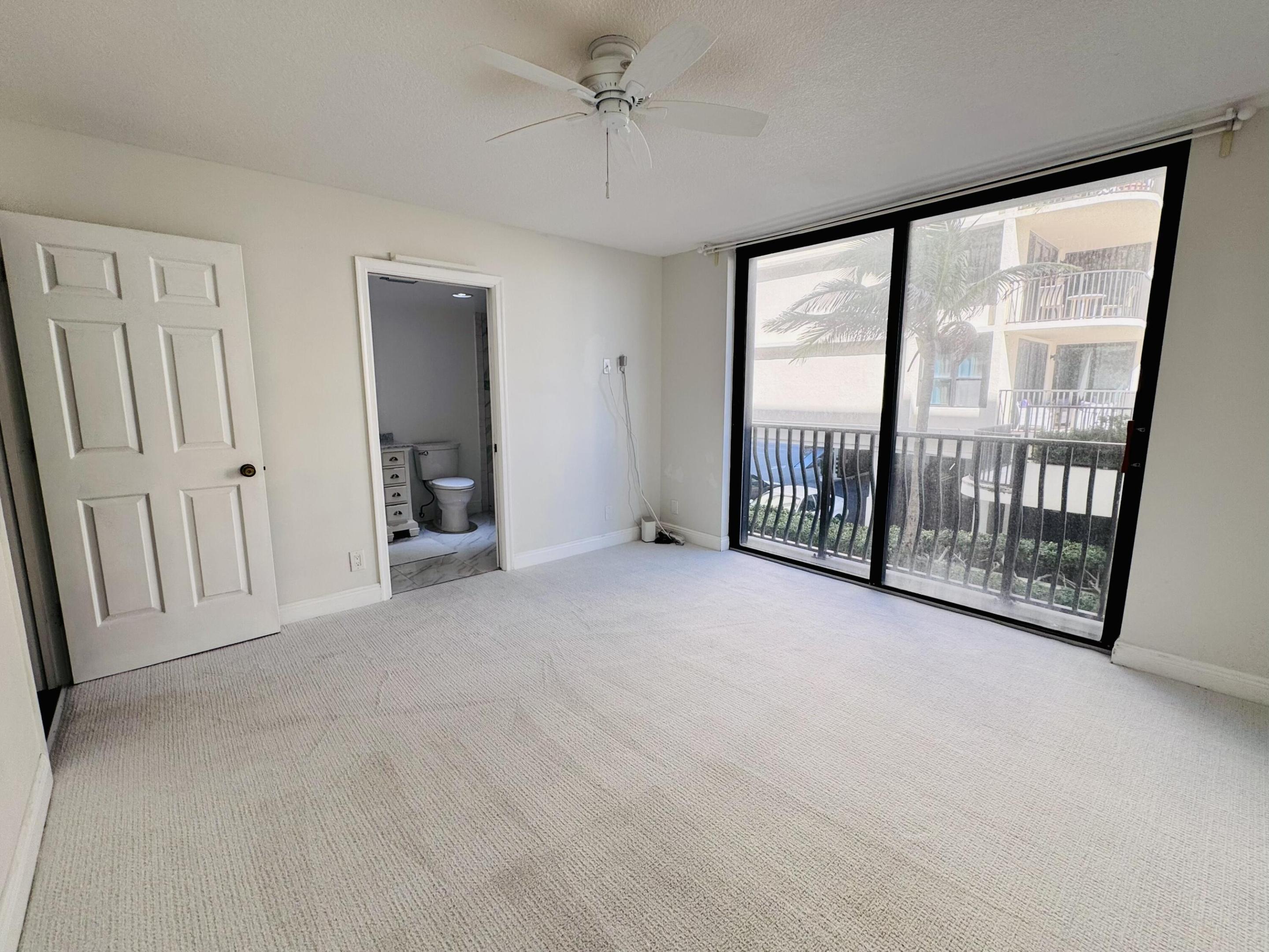 Interior space featuring neutral wall-to-wall carpeting, a ceiling fan, and floor-to-ceiling sliding glass doors with balcony access