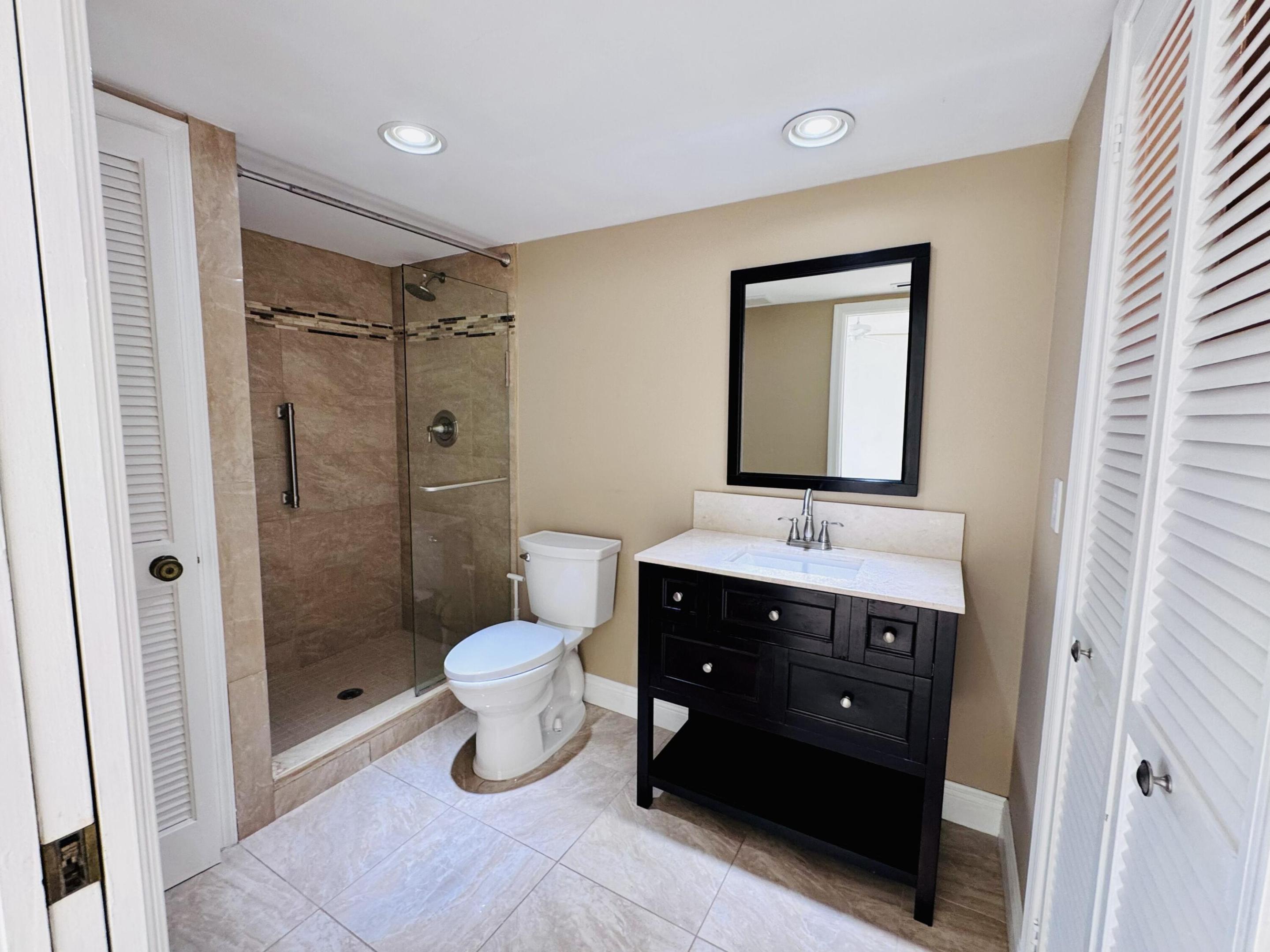 Bathroom featuring a walk-in shower with glass enclosure, vanity with stone-top basin, framed mirror, recessed lighting, and louvered-door closets