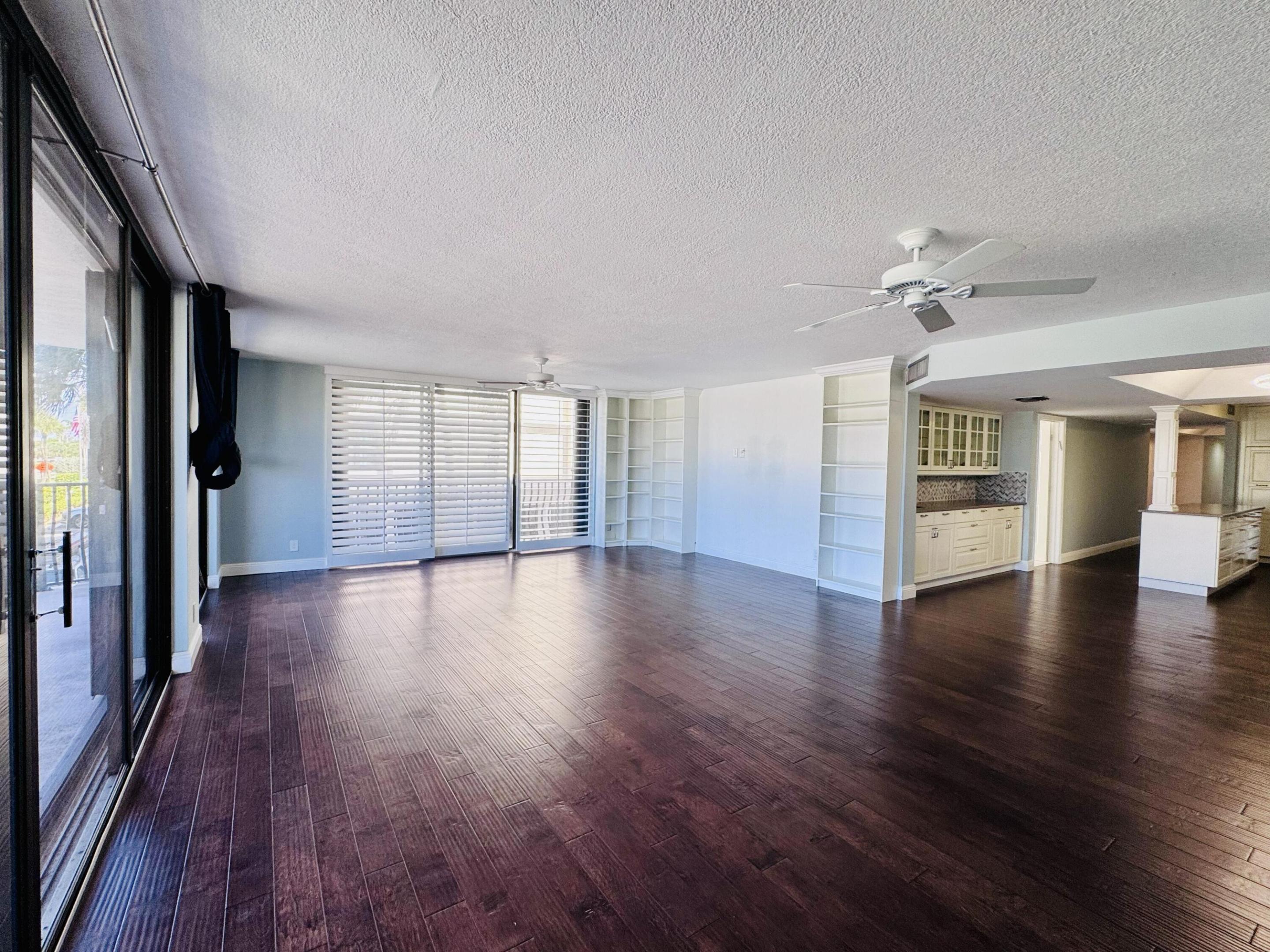 Expansive living area featuring wood-finish flooring, built-in shelving, glass sliding doors, and ceiling fans