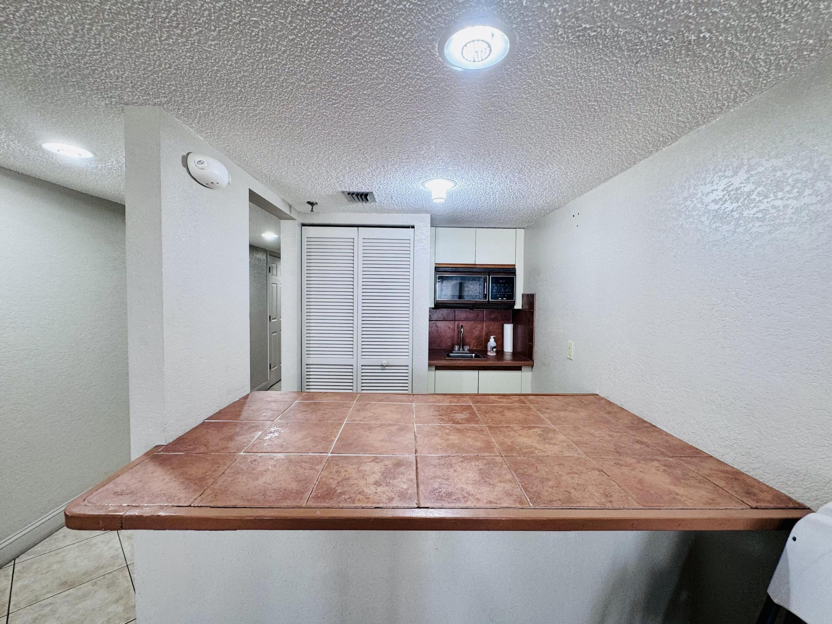 Tiled countertop peninsula with an integrated sink, built-in cabinetry, overhead microwave, and louvered closet doors