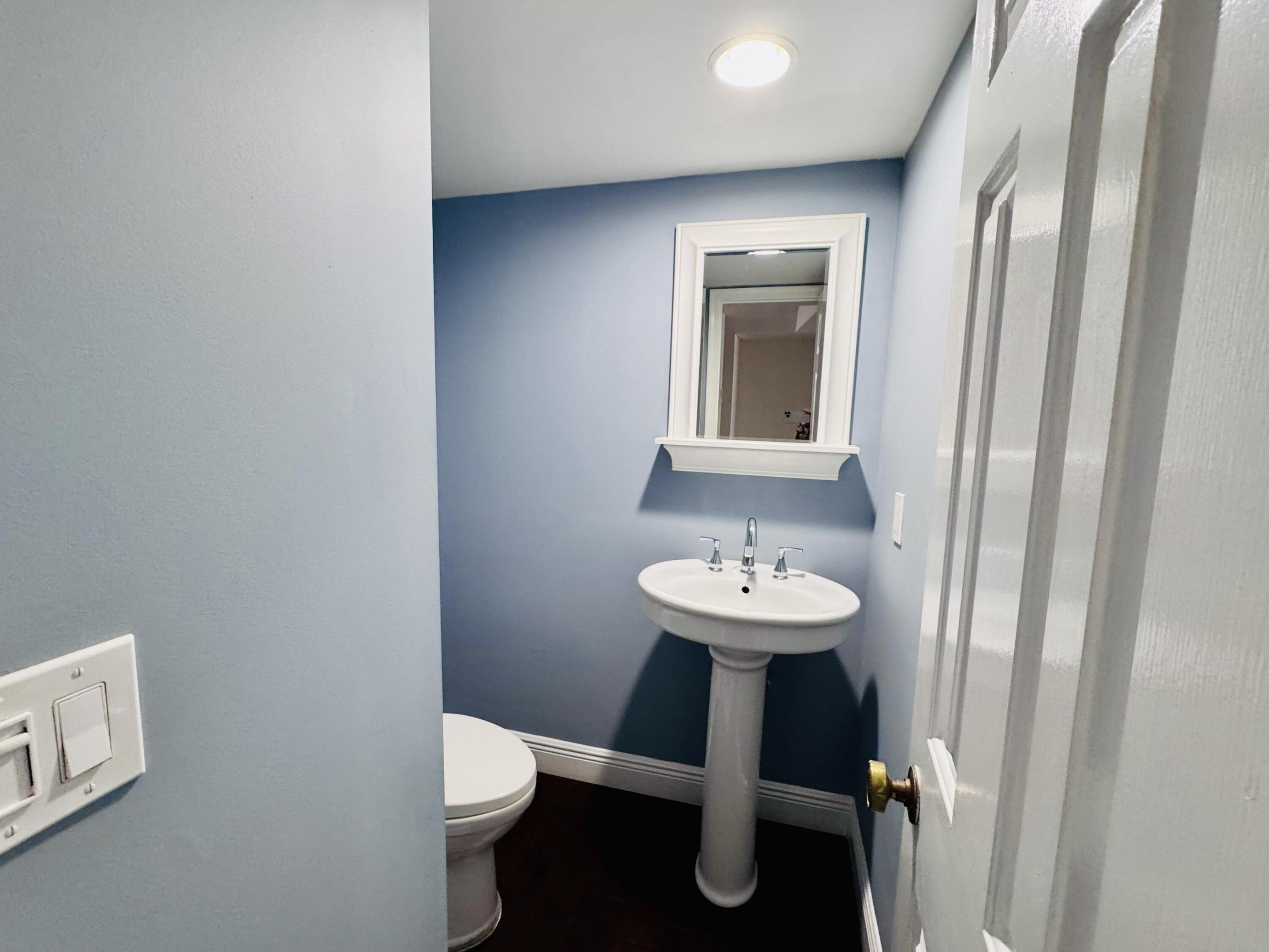 White porcelain pedestal sink with a dual-handle chrome faucet, framed wall mirror, and dark wood-finish flooring White porcelain pedestal sink with a dual-handle chrome faucet, framed wall mirror, and dark wood-finish flooring