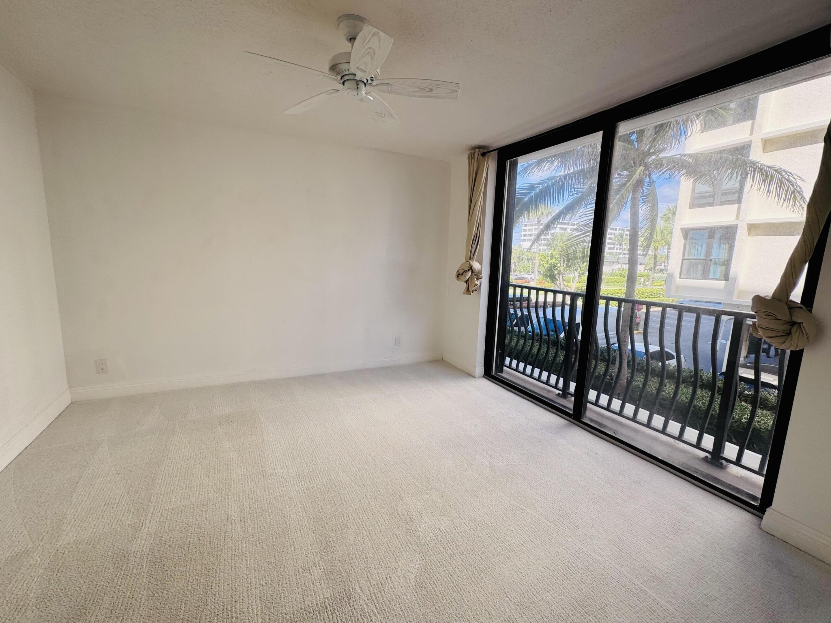 Interior space featuring neutral carpeting, a ceiling fan, and floor-to-ceiling sliding glass doors opening to a balcony with black metal railings