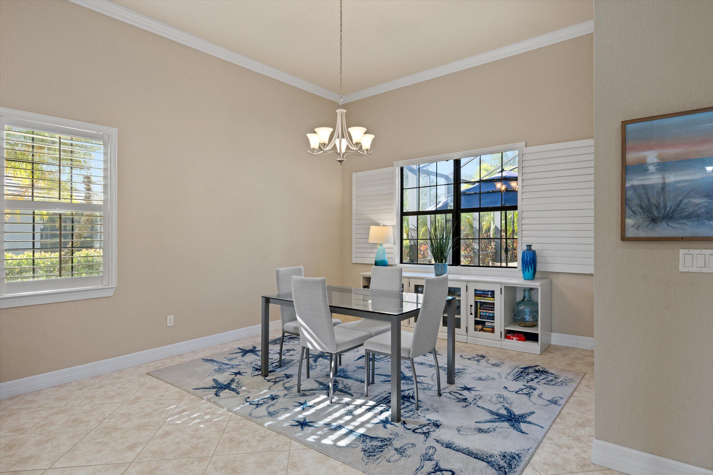 Dining area featuring high ceilings, crown molding, multi-pane windows with plantation shutters, a decorative chandelier, and tile flooring