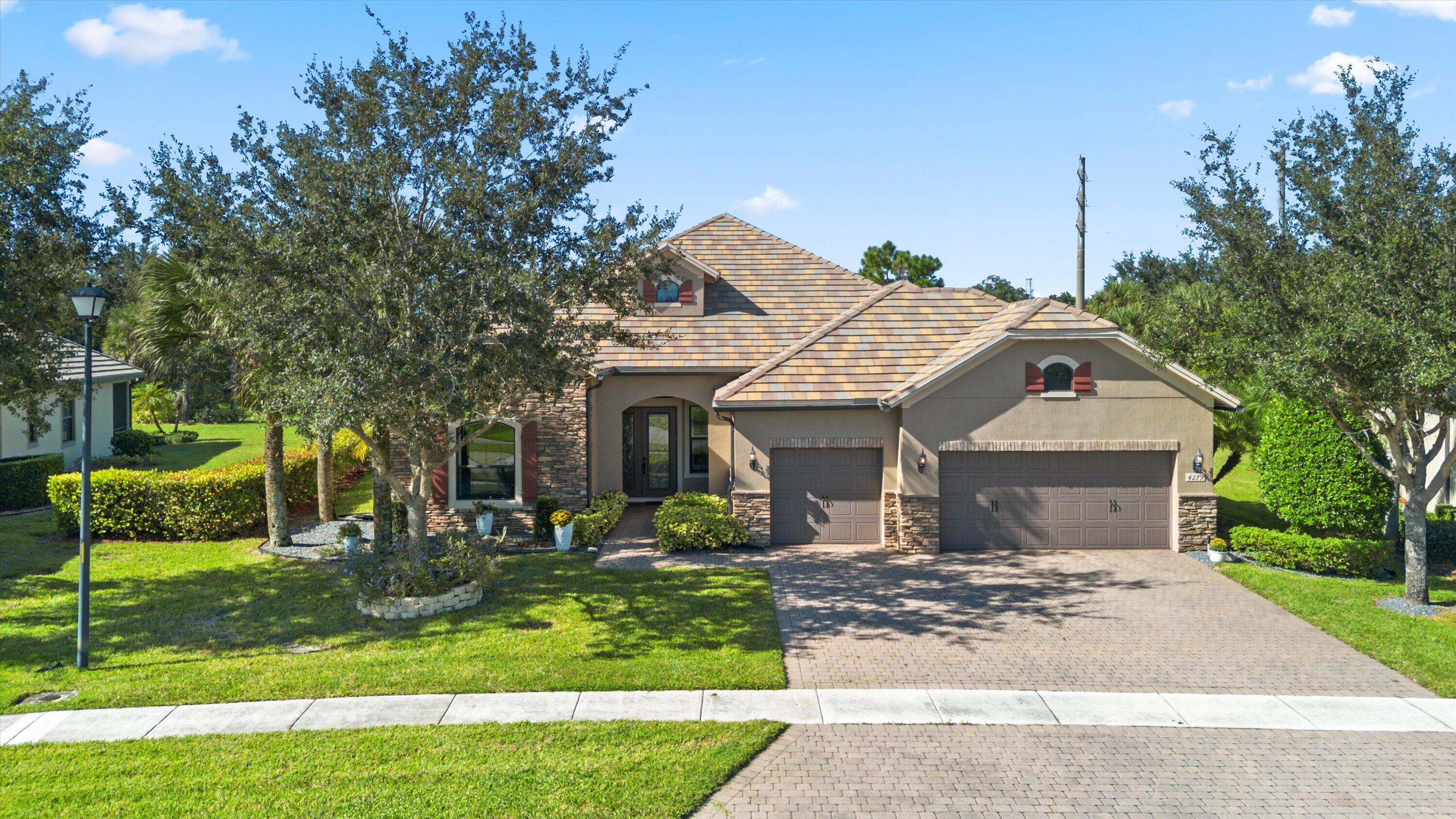 Stucco exterior residence featuring stone veneer accents, a multi-car garage, a paver driveway, and a tiled roof Stucco exterior residence featuring stone veneer accents, a multi-car garage, a paver driveway, and a tiled roof