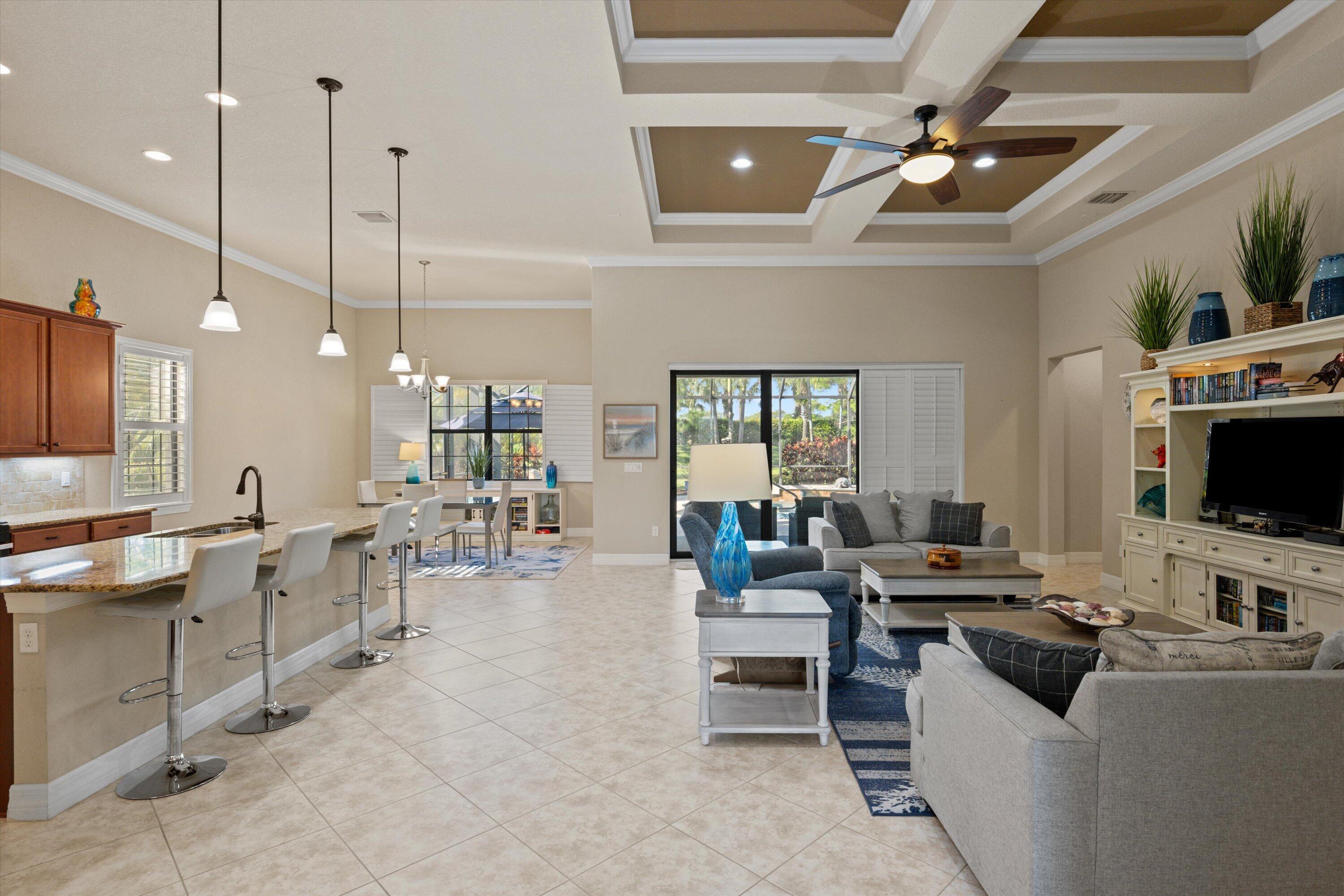 Open-concept layout featuring a coffered ceiling, recessed lighting, tile flooring, built-in entertainment cabinetry, and a kitchen island with pendant lighting