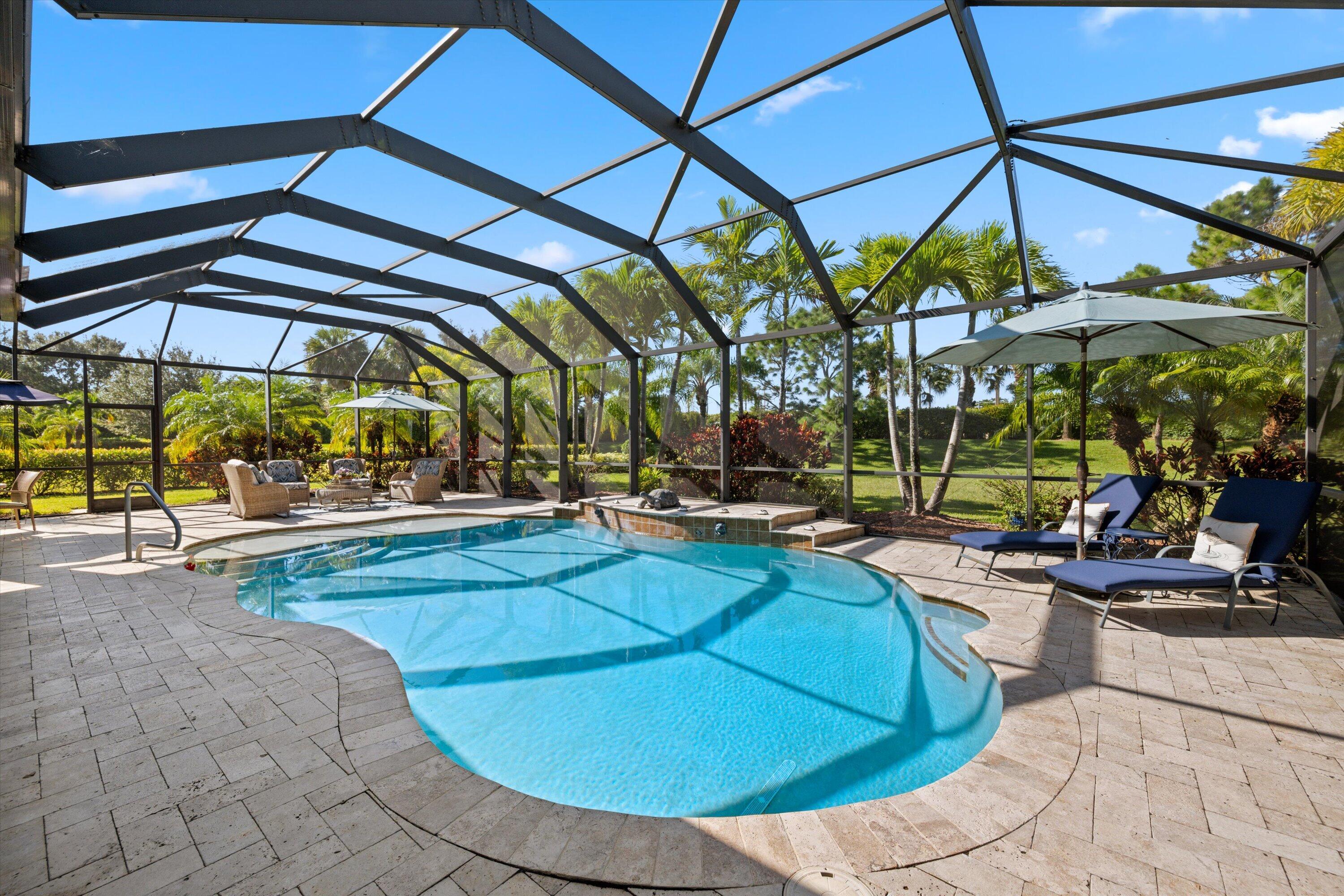 Screen-enclosed pool area featuring an in-ground pool, elevated spa, and stone-paver decking