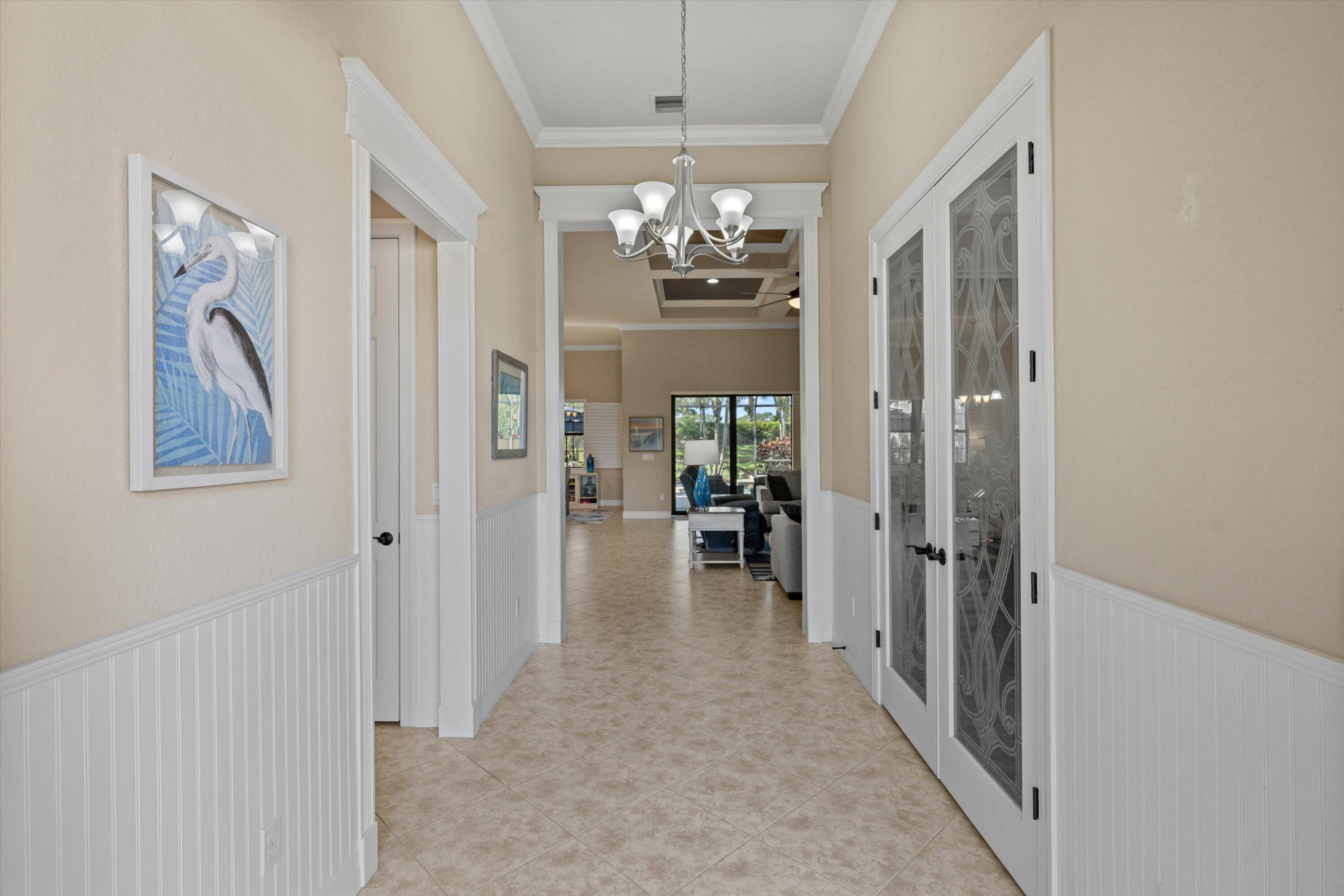 Foyer featuring white beadboard wainscoting, crown molding, tile flooring, a multi-arm chandelier, and glass-paneled French doors with decorative etched detailing Foyer featuring white beadboard wainscoting, crown molding, tile flooring, a multi-arm chandelier, and glass-paneled French doors with decorative etched detailing