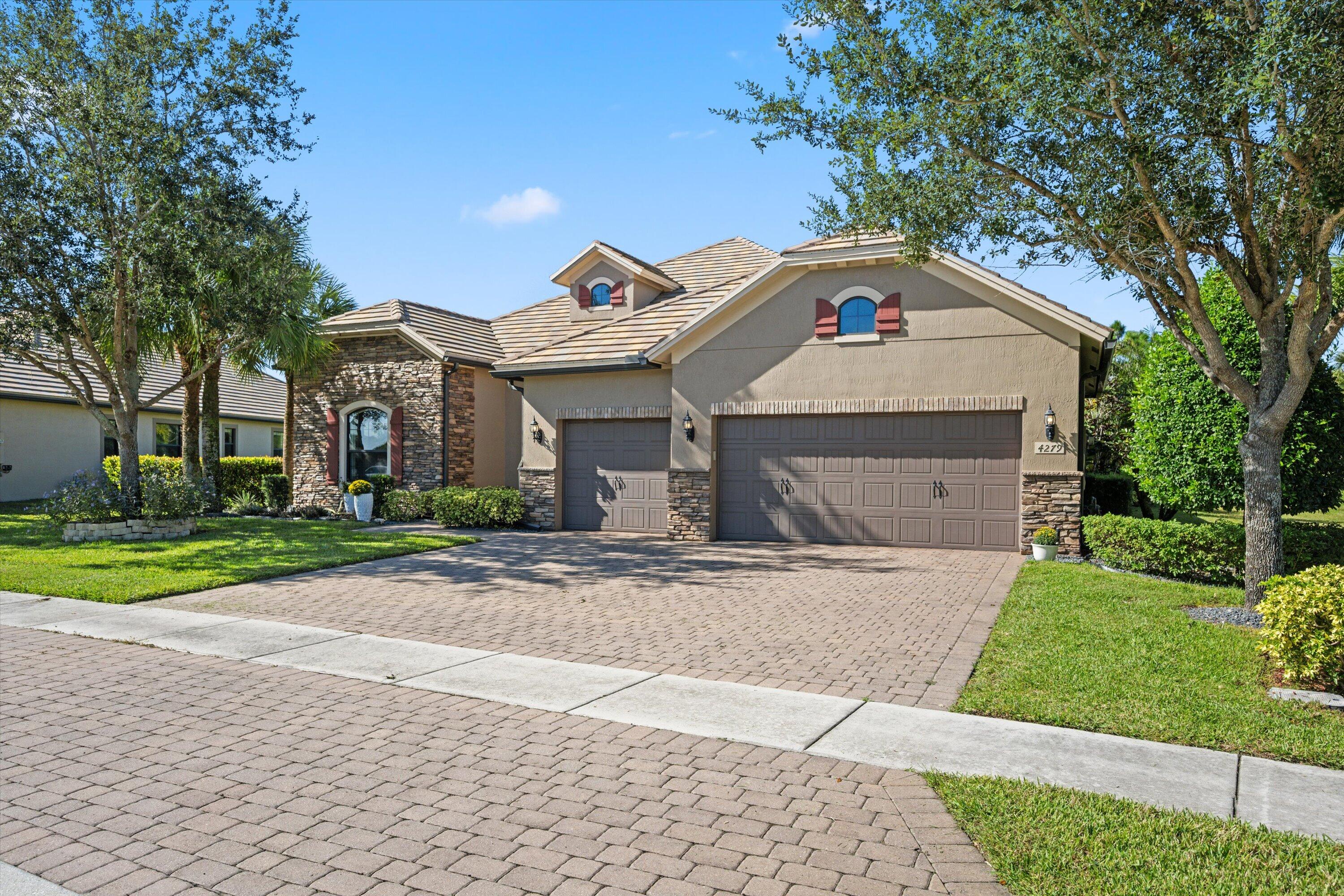 Stucco exterior featuring stone veneer accents, multi-gabled roofline, arched window detailing, three-car garage, and paved driveway Stucco exterior featuring stone veneer accents, multi-gabled roofline, arched window detailing, three-car garage, and paved driveway