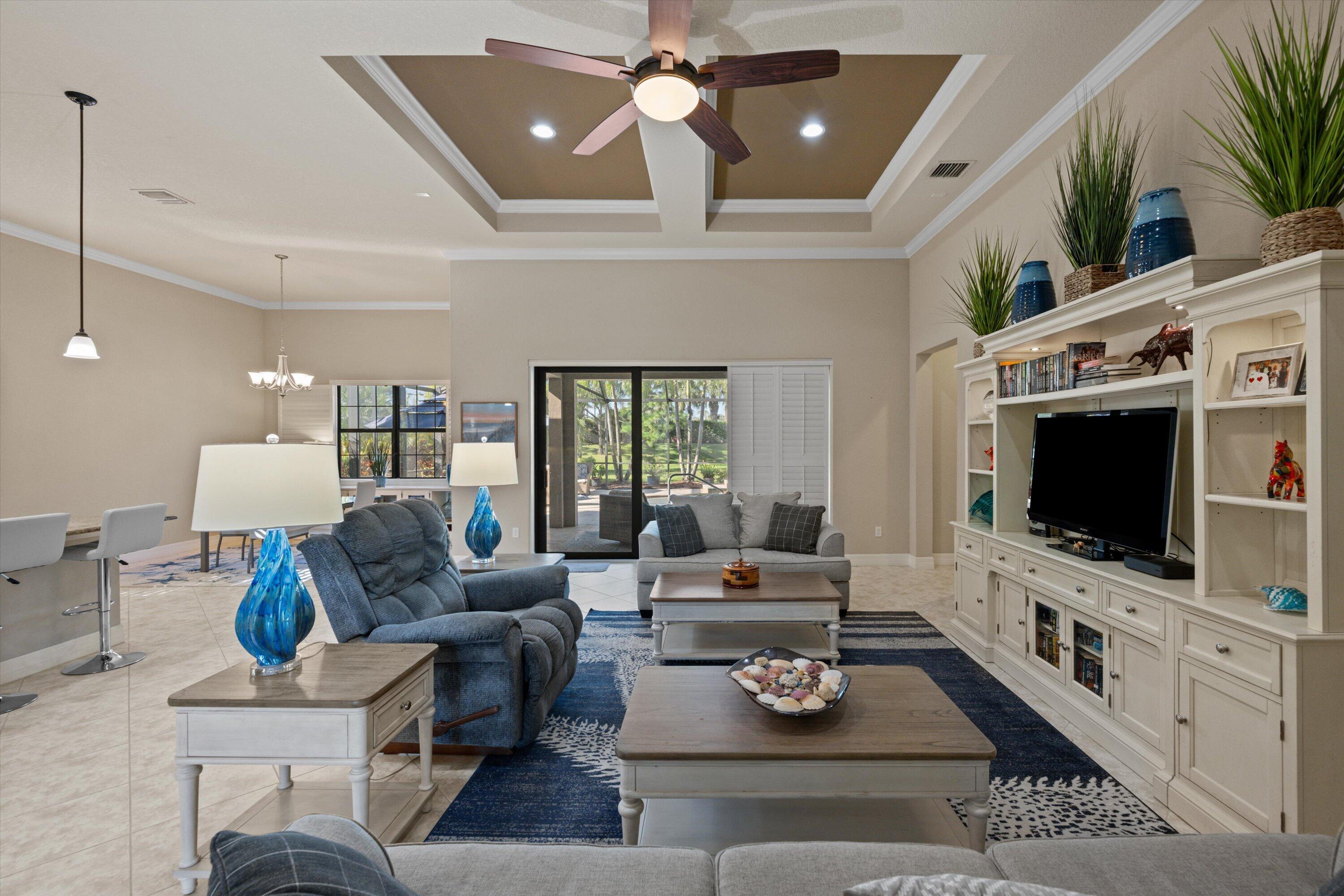 Coffered ceiling with recessed lighting, central ceiling fan, built-in floor-to-ceiling media cabinetry, tile flooring, and sliding glass doors Coffered ceiling with recessed lighting, central ceiling fan, built-in floor-to-ceiling media cabinetry, tile flooring, and sliding glass doors