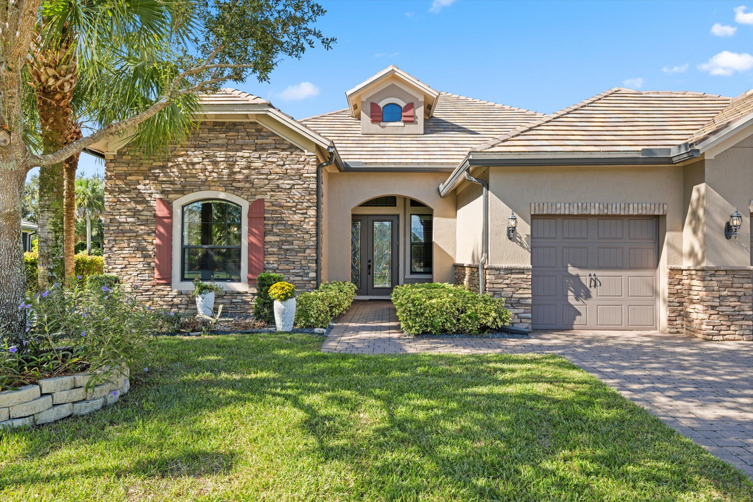 Single-story residence featuring a stone veneer and stucco facade, arched entryway, decorative shutters, and a paver driveway Single-story residence featuring a stone veneer and stucco facade, arched entryway, decorative shutters, and a paver driveway