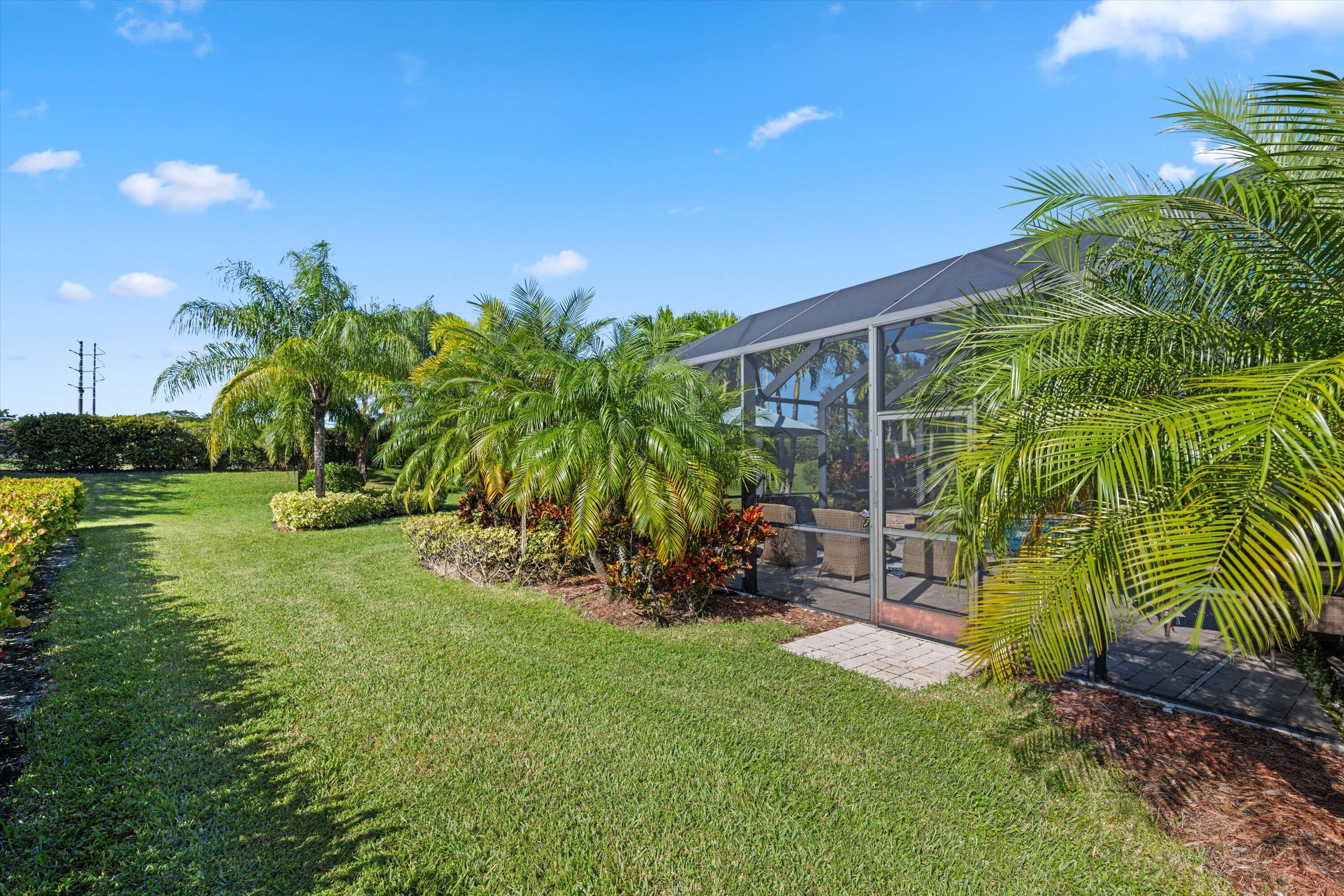 Screened-in patio enclosure featuring paver accent landing, surrounded by mature palms, manicured lawn, and professional landscape shrubbery