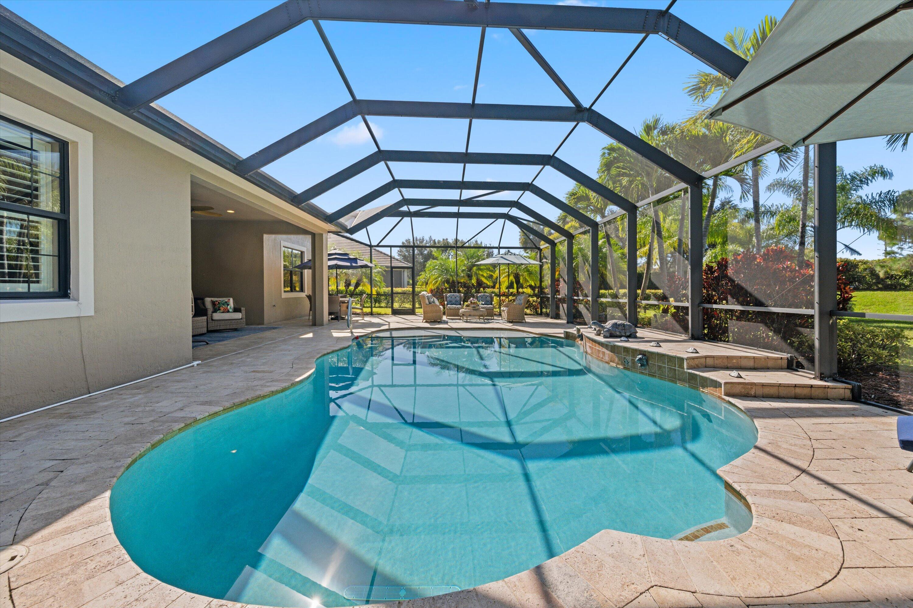 Screened-in patio featuring a custom-shaped pool, raised spillover spa, stone-finish decking, and exterior house access