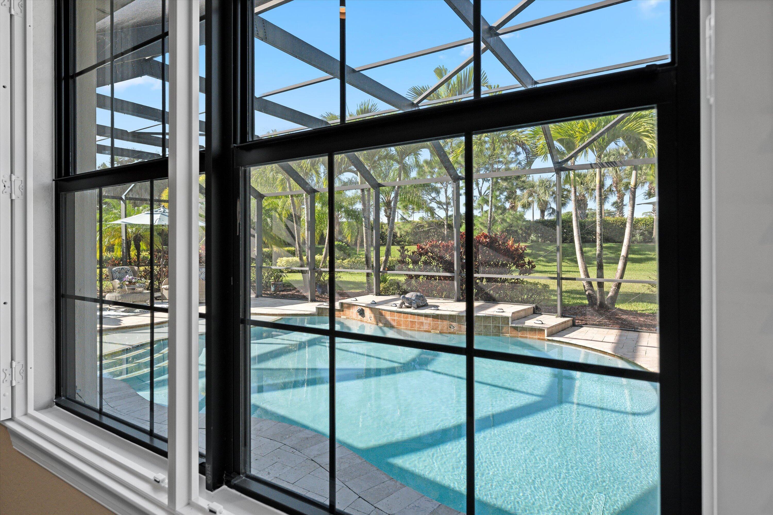 View from Primary. Grid-pattern windows with black frames, screen-enclosed pool, spa, and paver decking