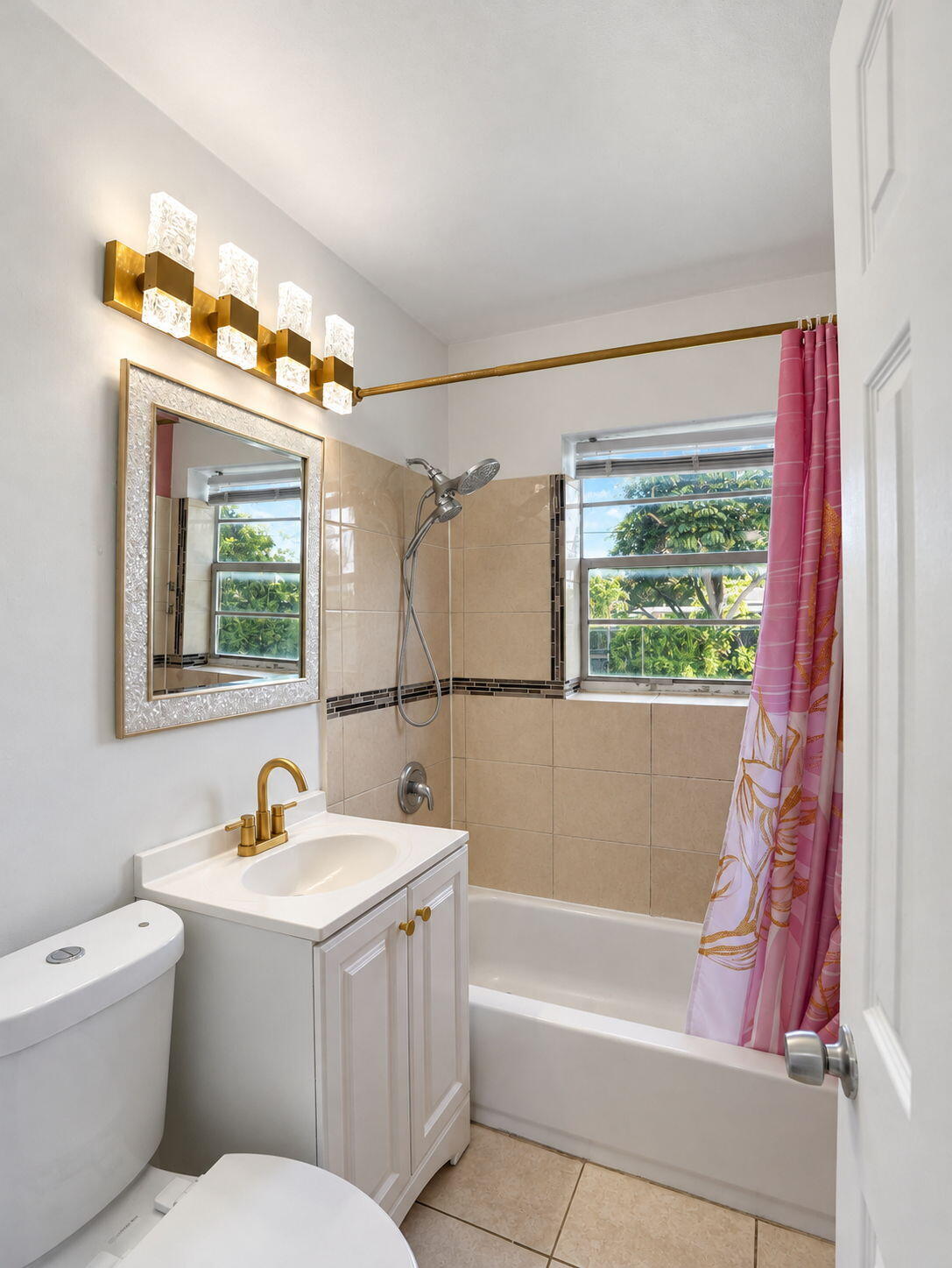 Bathroom featuring a white vanity with brass-finish faucet, multi-light fixture, combo shower/tub