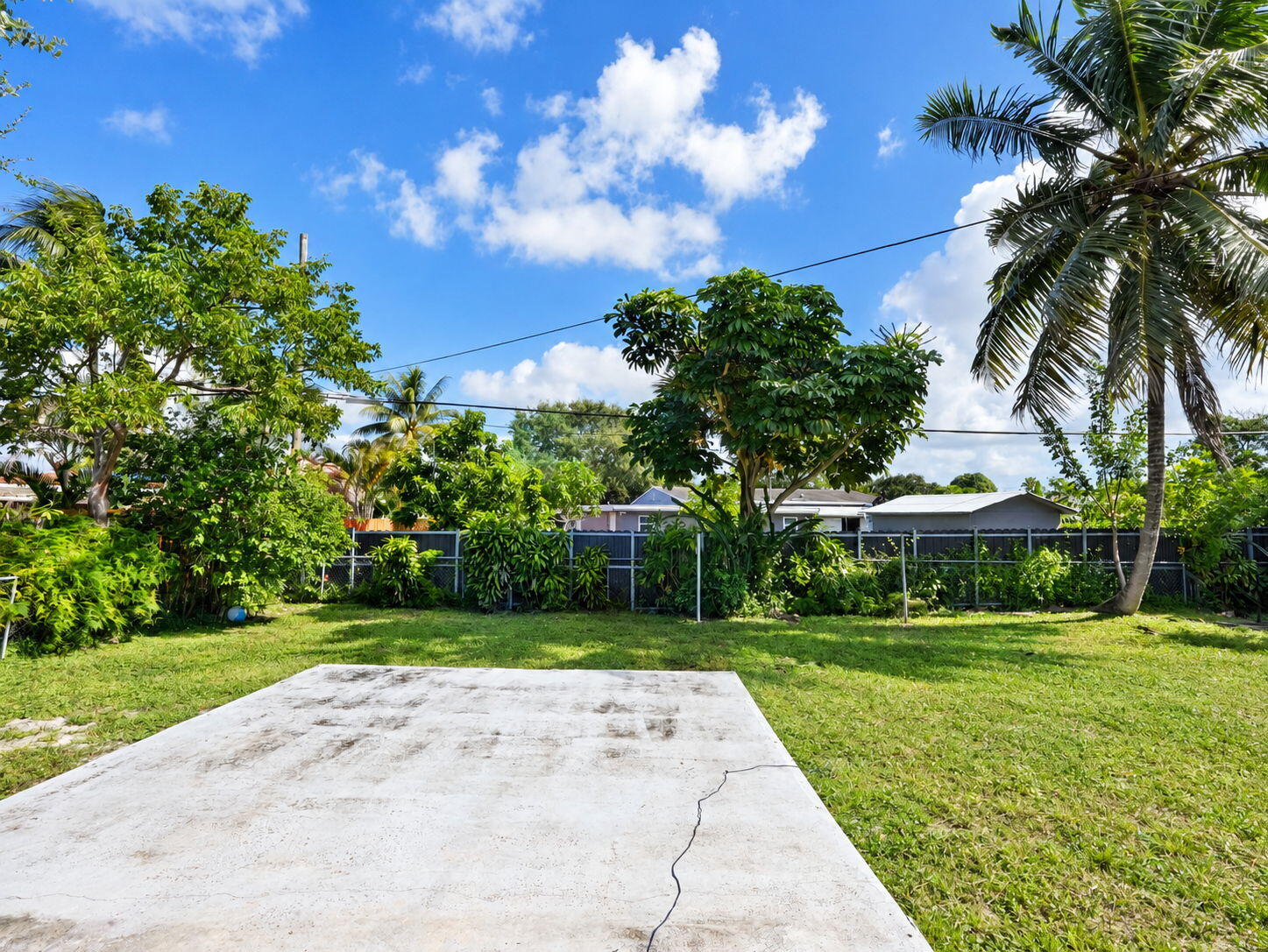 Expansive backyard featuring a concrete patio, mature trees, and perimeter fencing