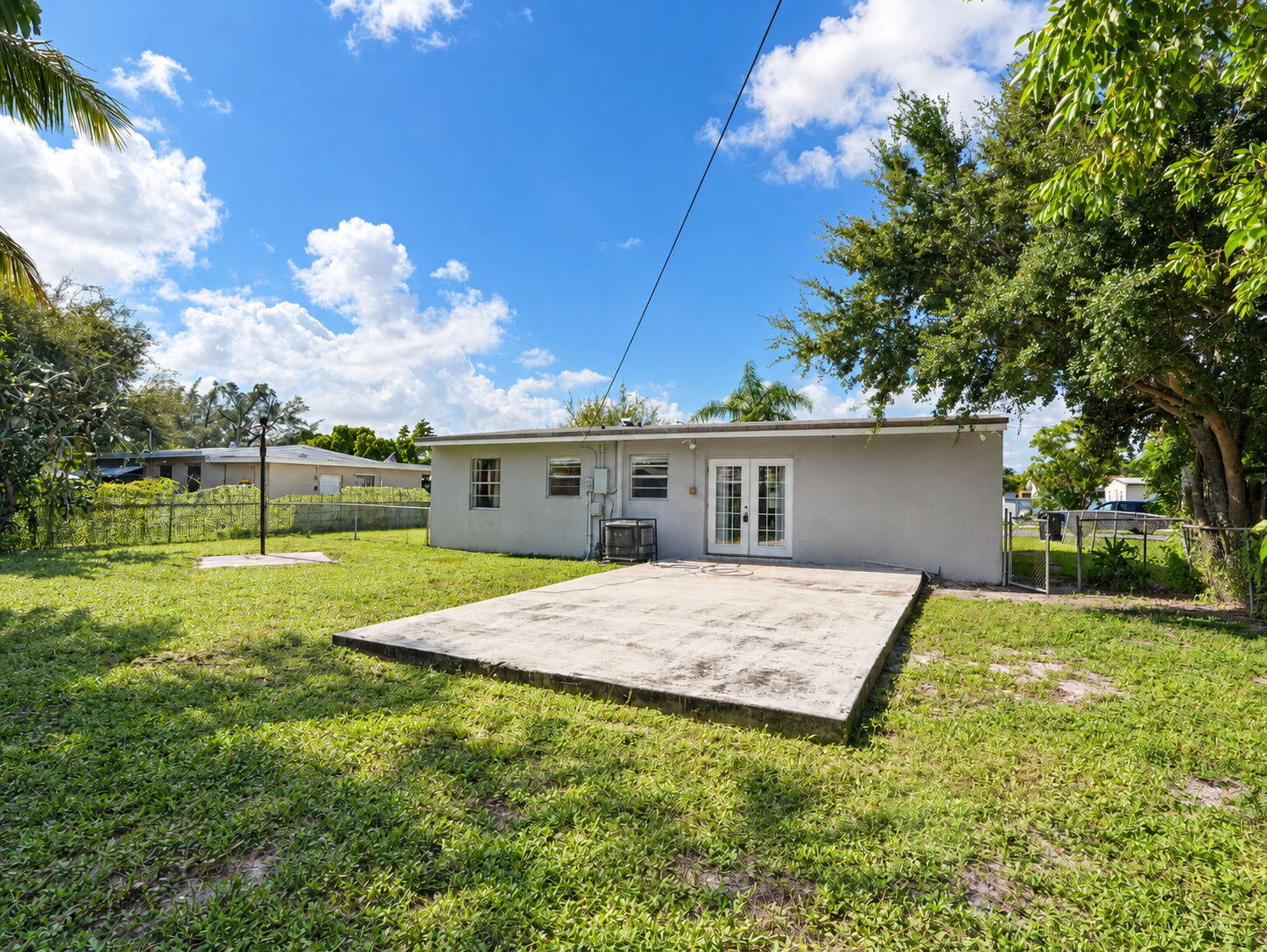 Rear exterior featuring a concrete patio, grassy yard, chain-link perimeter fencing, and double glass-panel doors