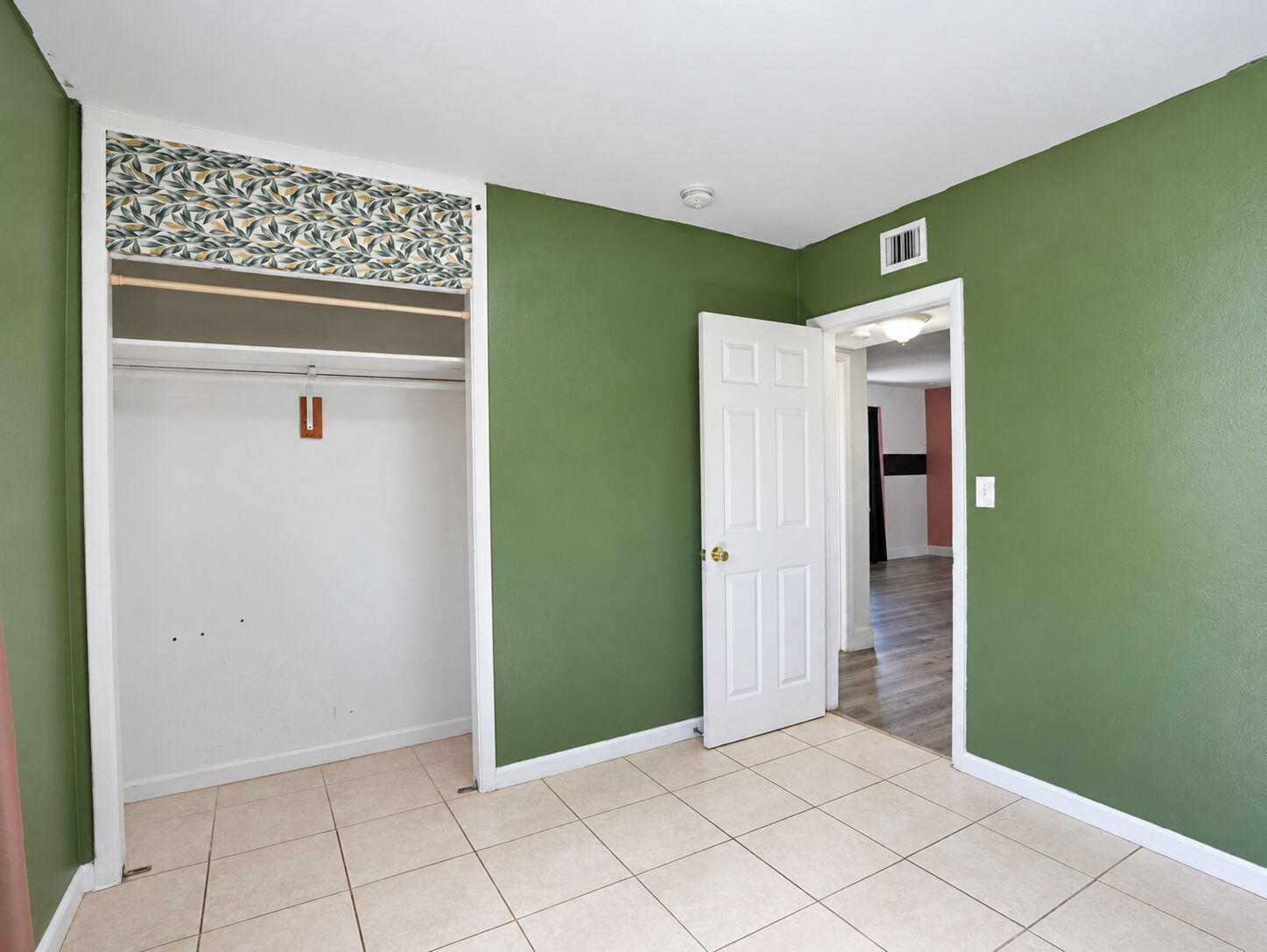 Bedroom interior featuring neutral tile flooring, six-panel interior door, and built-in closet with decorative valance