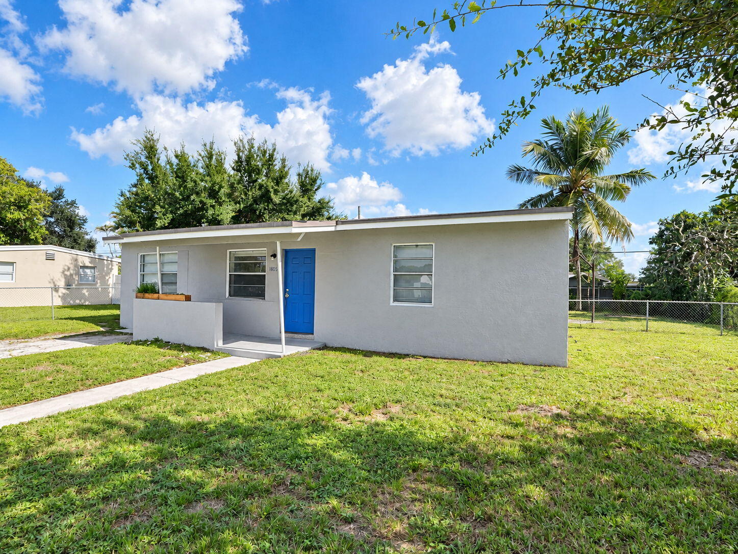 Single-story exterior featuring a neutral stucco facade, blue entry door, horizontal sliding windows, and a concrete walkway