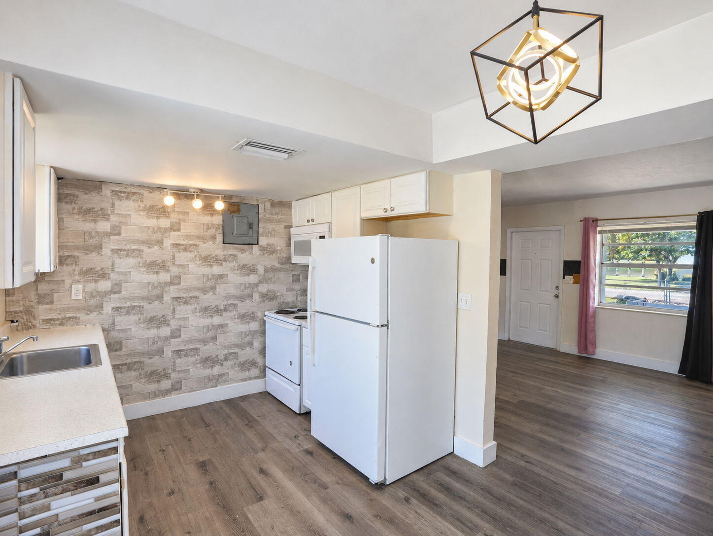 Kitchen featuring wood-finish flooring, white cabinetry, integrated geometric pendant lighting, and a neutral-toned countertop