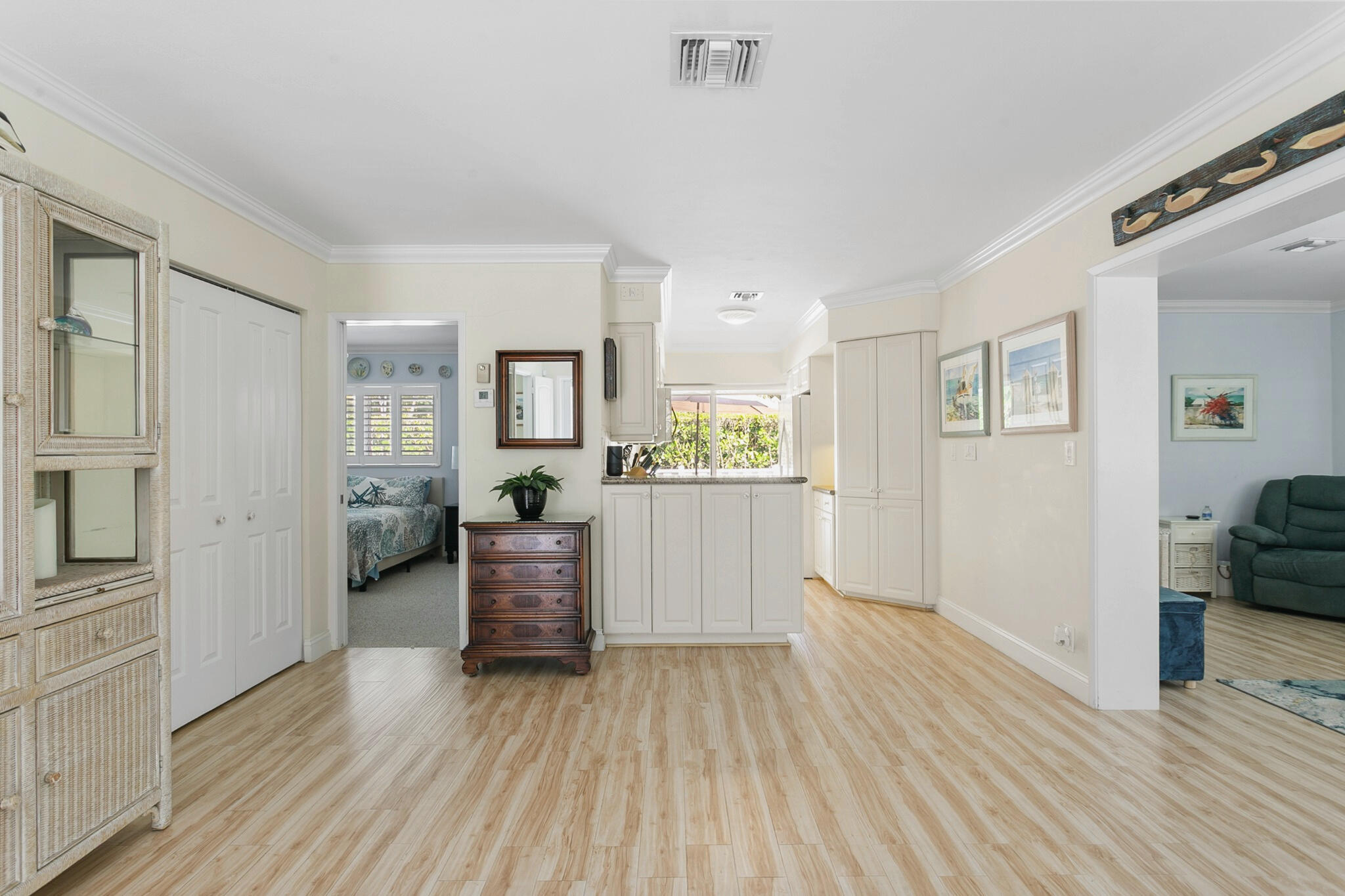 Open-concept interior featuring light-toned wood-finish flooring, white cabinetry with crown molding, and recessed lighting
