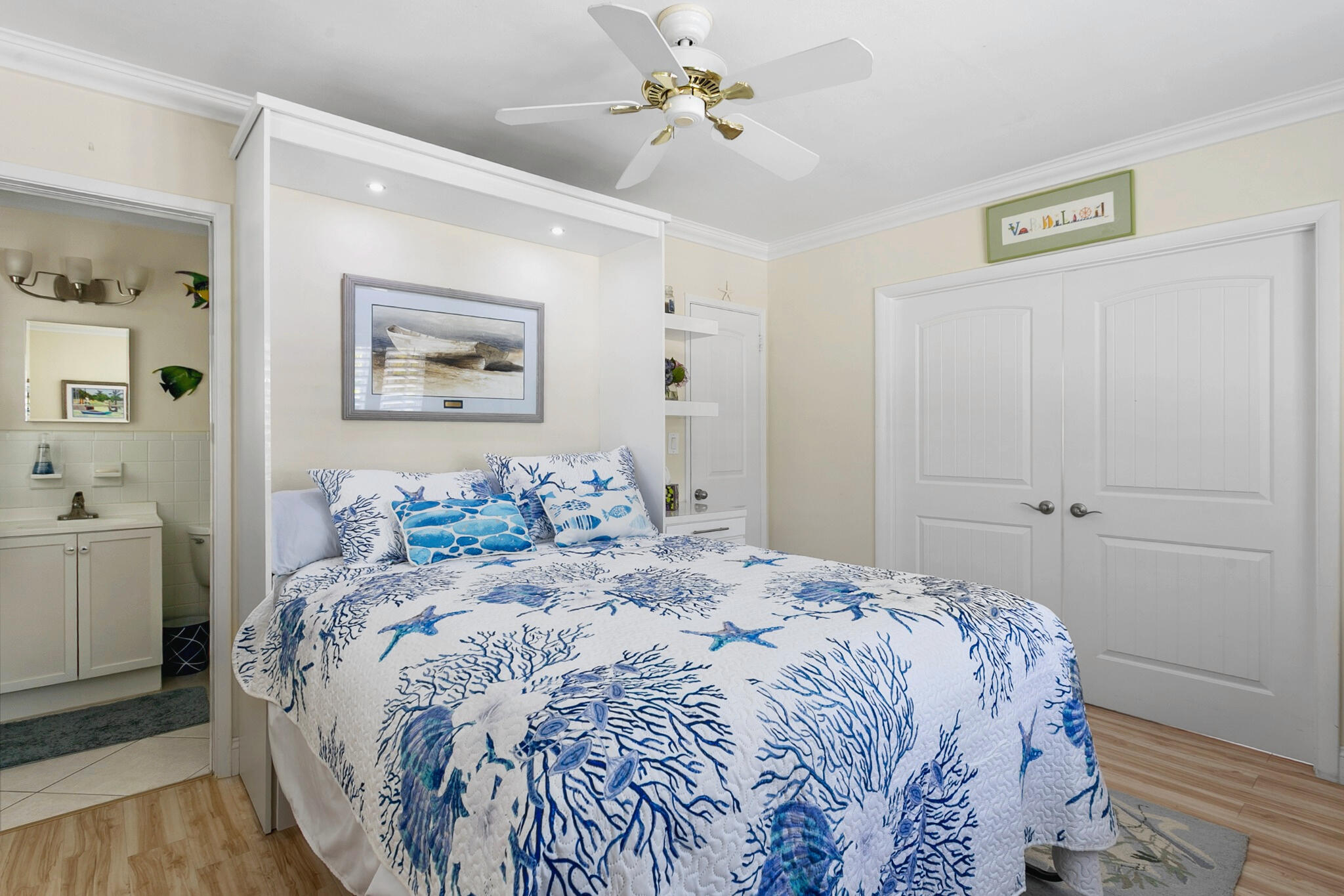 Murphy bed with integrated lighting, double-door closet, crown molding, white ceiling fan, and wood-finish flooring