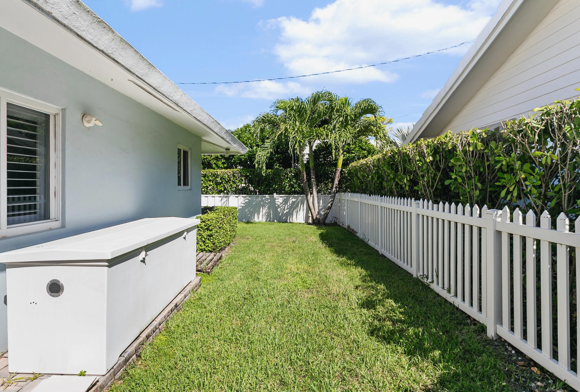 Side yard featuring a manicured lawn, white picket fencing, structured hedge landscaping. Ideal area for pets to play and roam