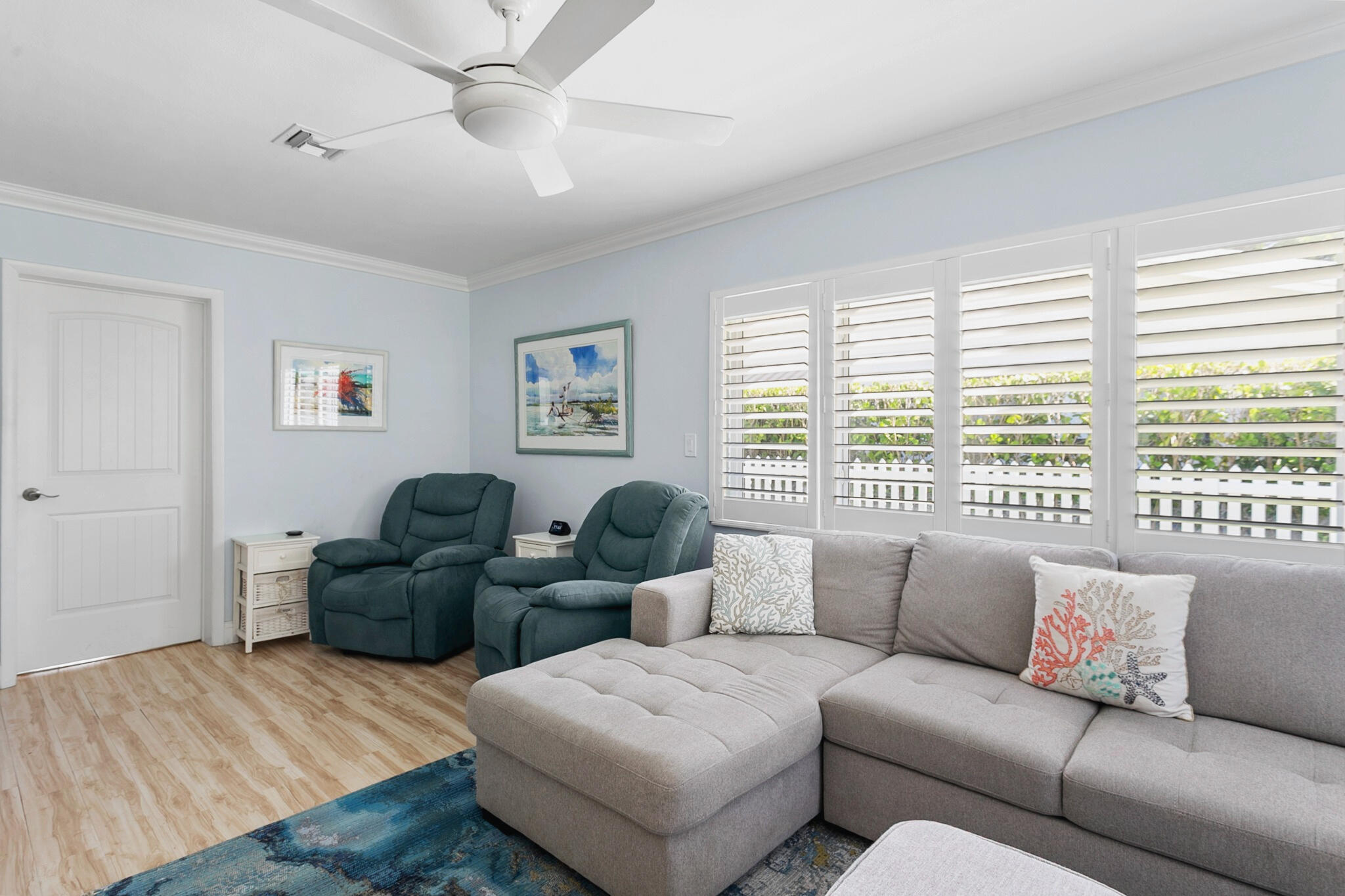 Light-filled living room featuring wood-finish flooring, plantation shutters, and a ceiling fan